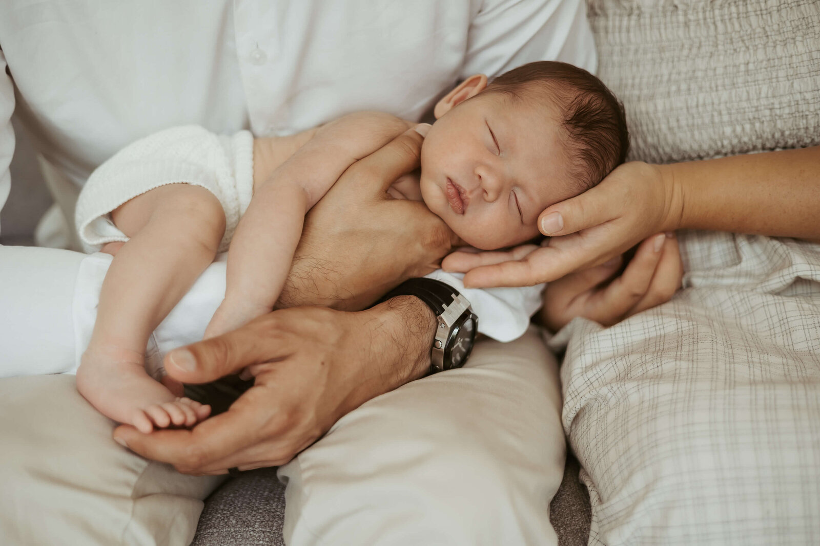 A little bub sleeping on his dad's lap and mum is  cradling his small head during their newborn photography experience.