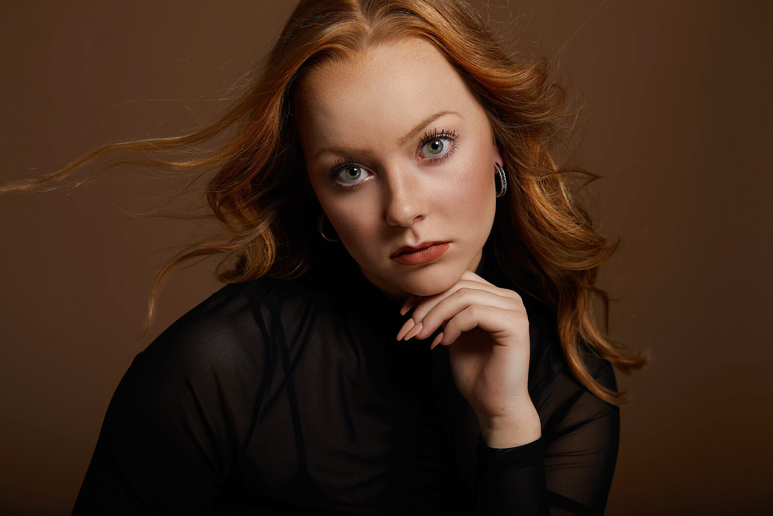 Red haired young woman at Studio 64 Photography posing for headshot with serious expression on brown backdrop.