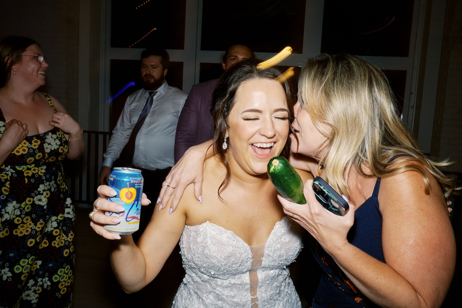 Bride laughs on the dance floor while a wedding guest whispers in her ear