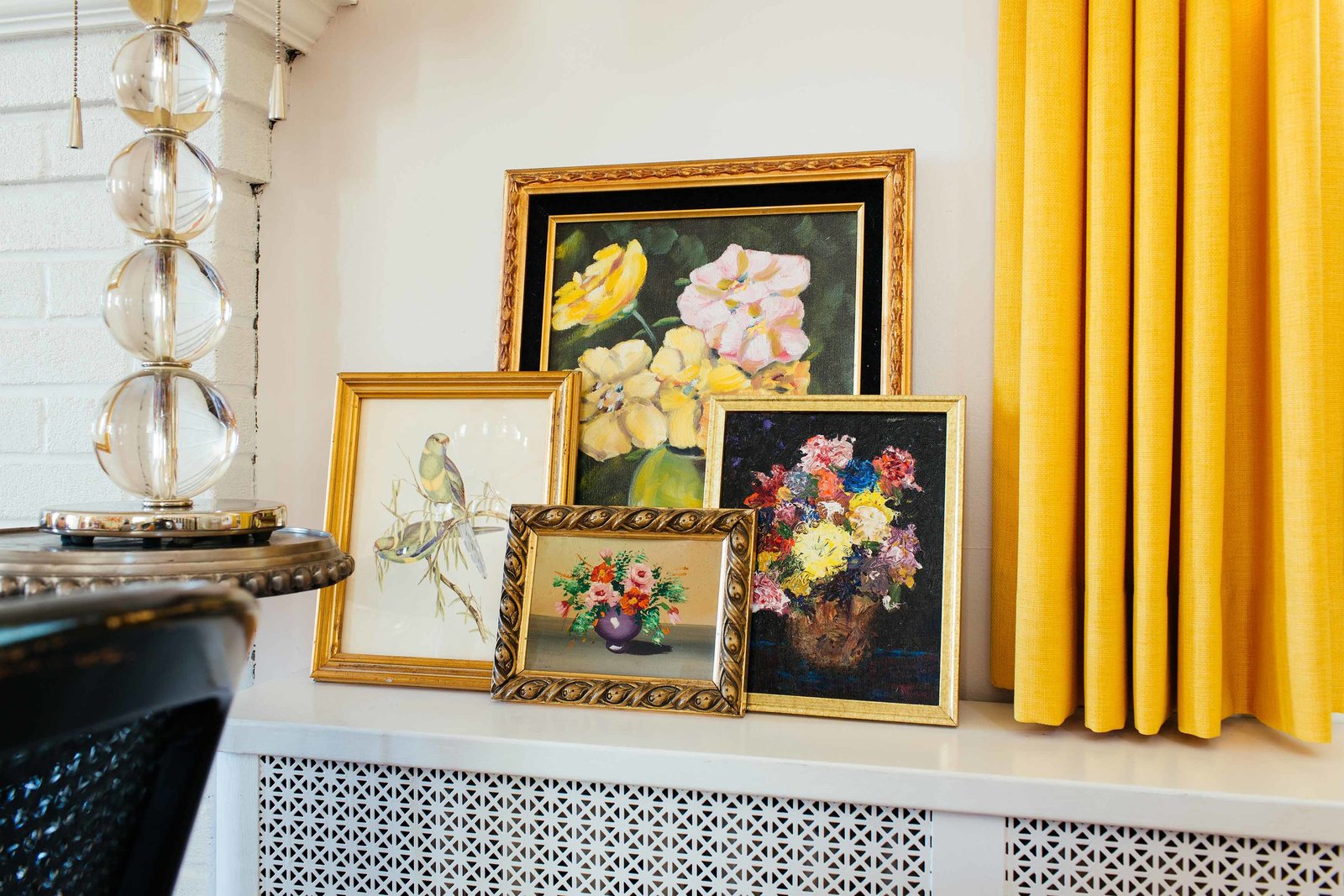 Four framed art prints on a shelf beside a yellow drape.