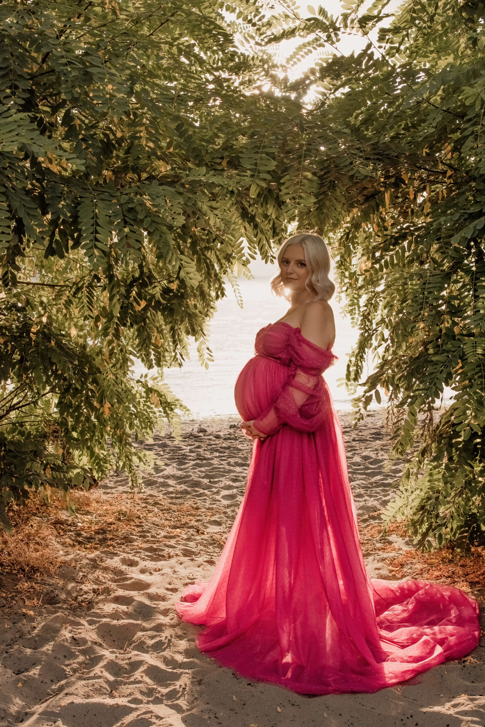 Pregnant woman in pink dress standing in the sun.