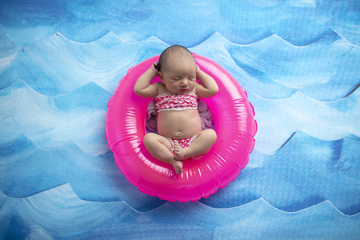Newborn girl in swimsuit on pink tube.