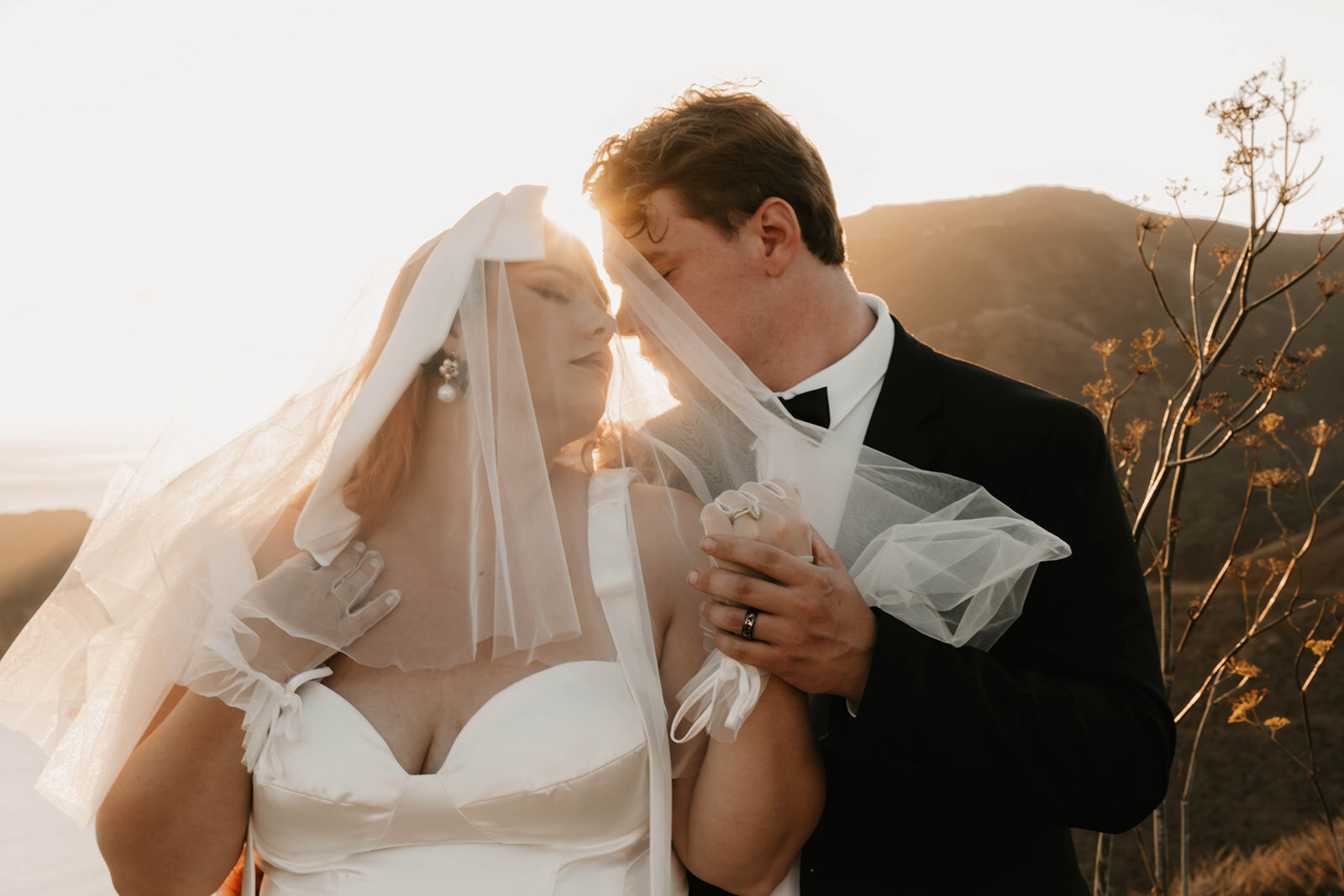Bride and groom under a veil, holding hands and sharing a tender moment at sunset—captured with candid wedding photography at golden hour during their Colorado wildflower elopement.