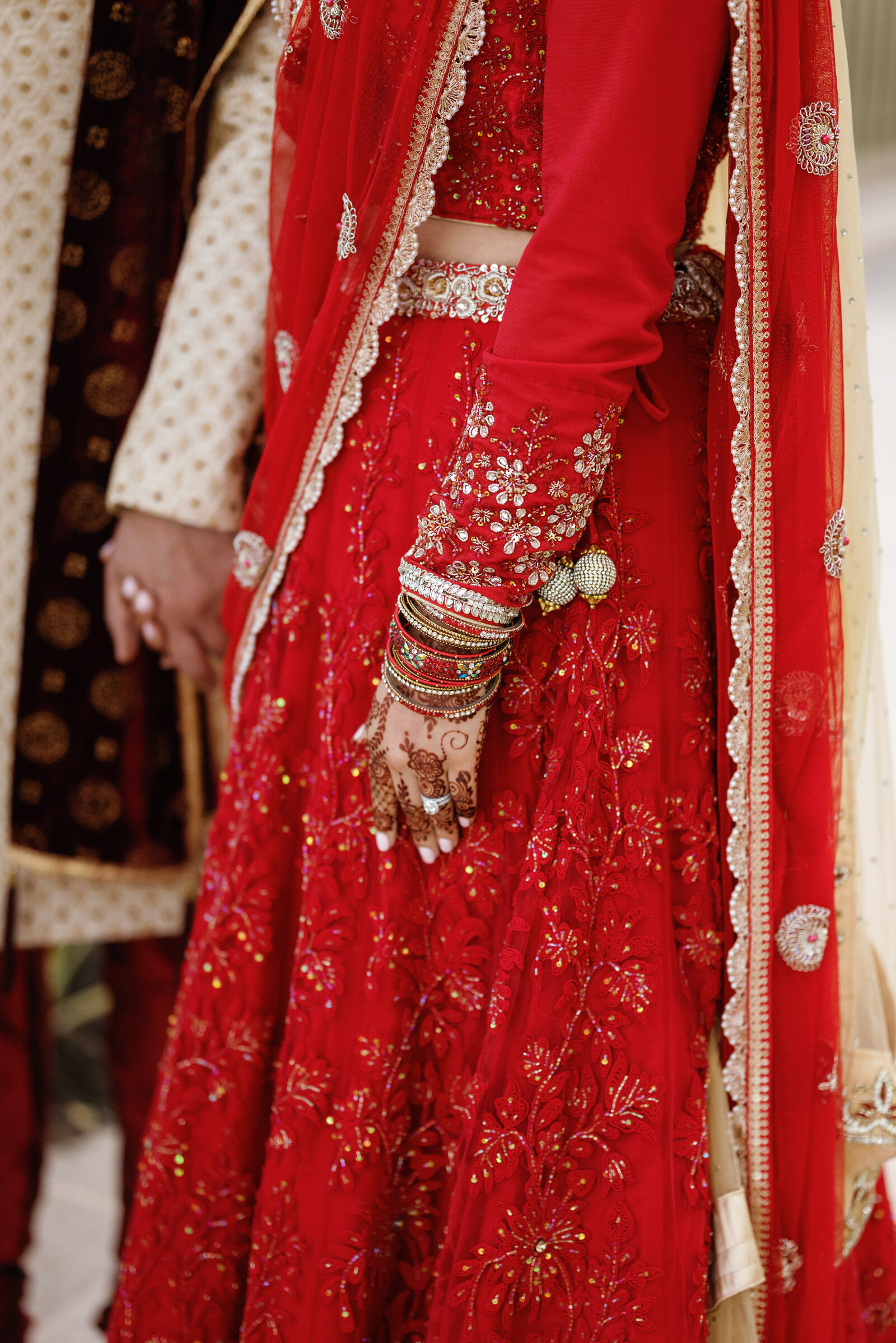 detail of Indian brides hand against her red sari. Her bracelets and the texture of her sari are on display