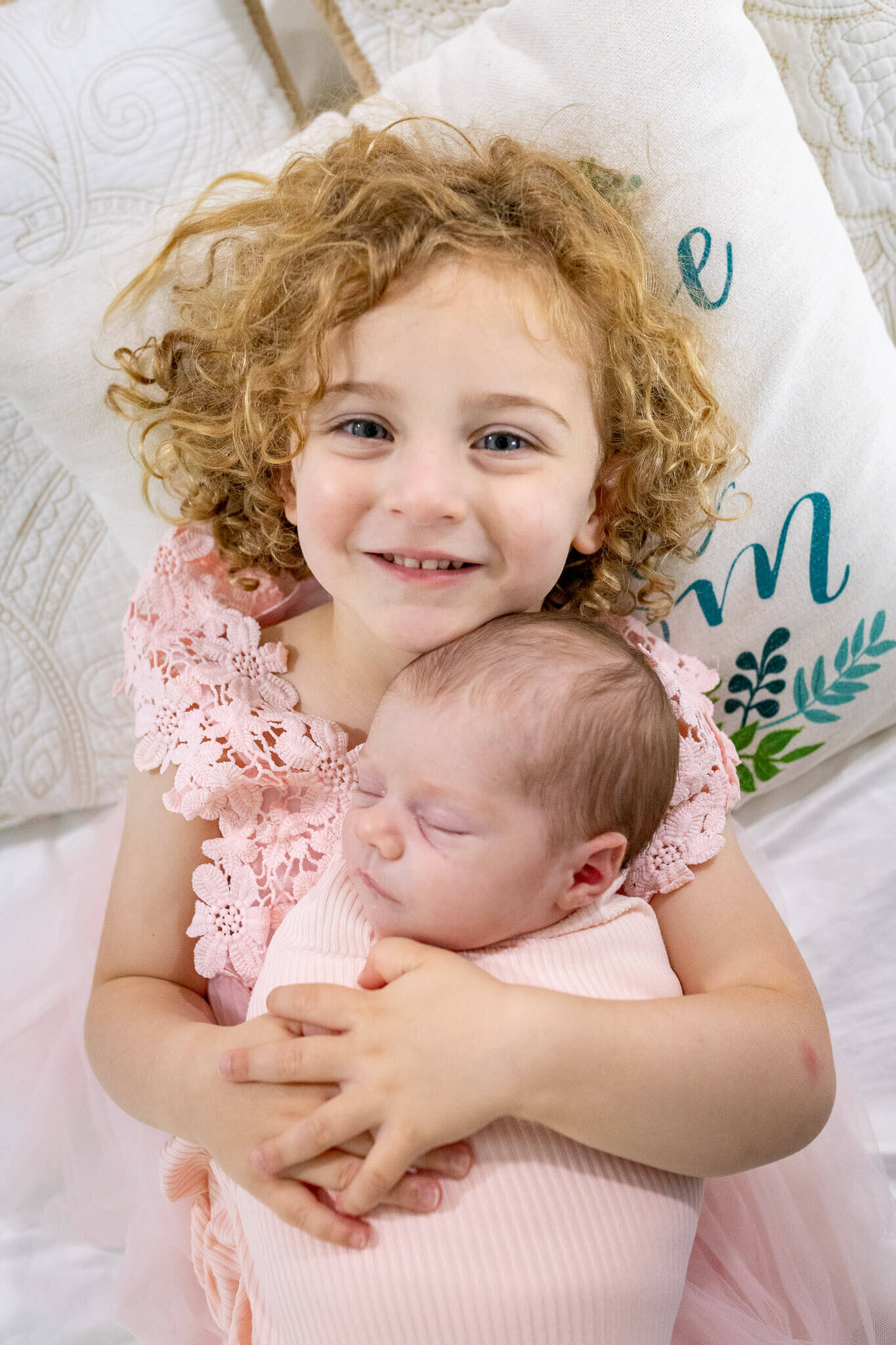 A close-up of big sister holding her baby sister in bed in their Alexandria home.