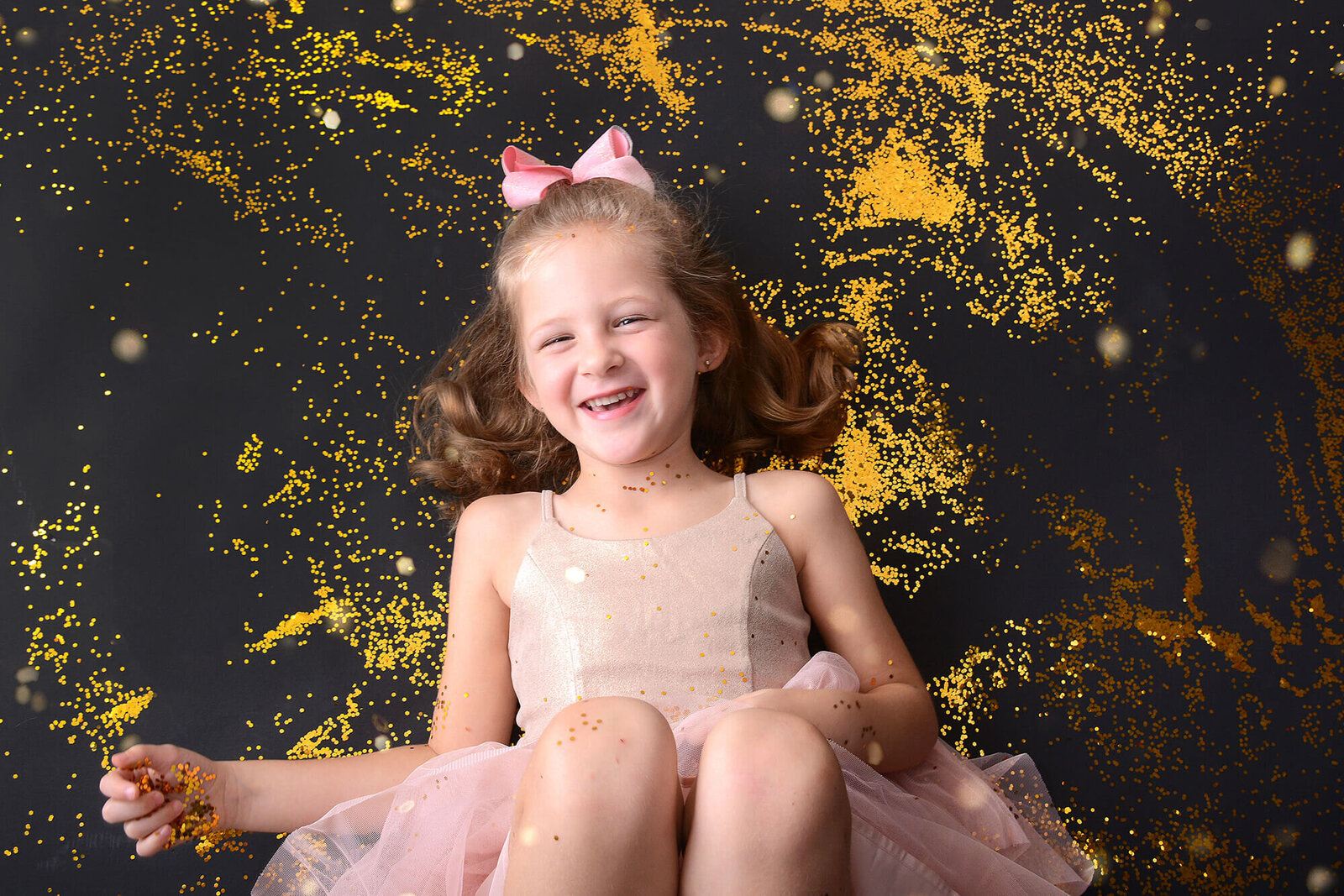 girl smiles on the ground covered in glitter at her glitter mini shoot in houston