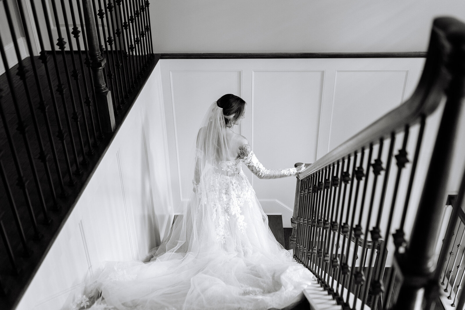 A black and white photo of a bride as she walks slowly down the stairs to meet her groom