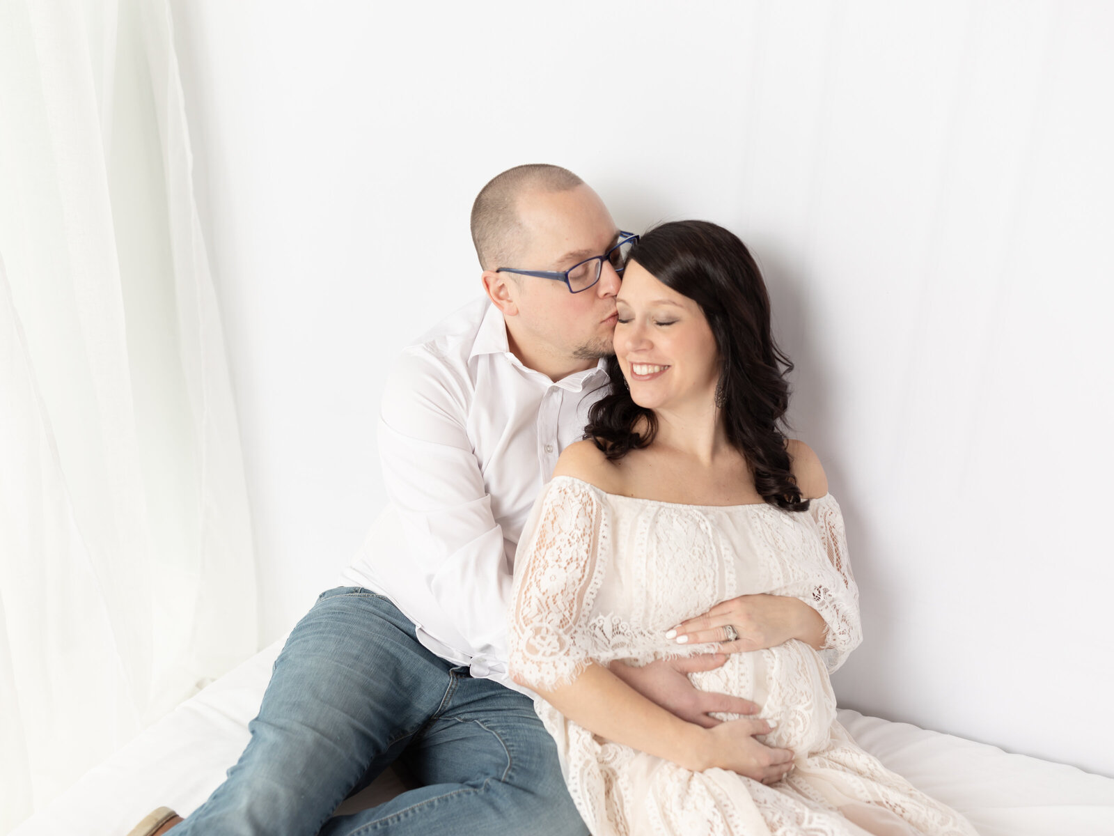 husband holding pregnant wife sitting on white bed cleveland maternity photographer