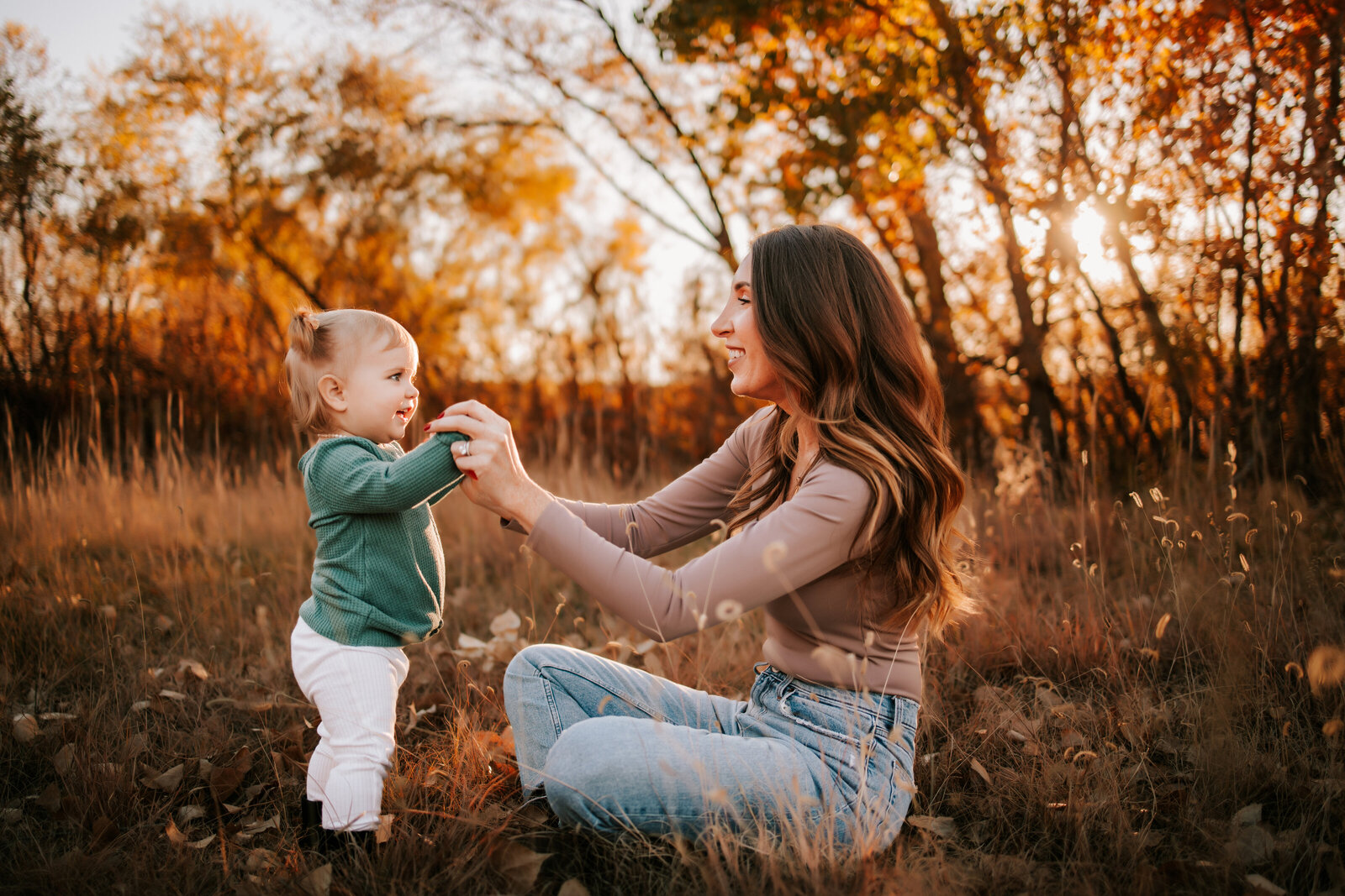 mom holds hands with toddler girl during family photos  in the fall golden hour