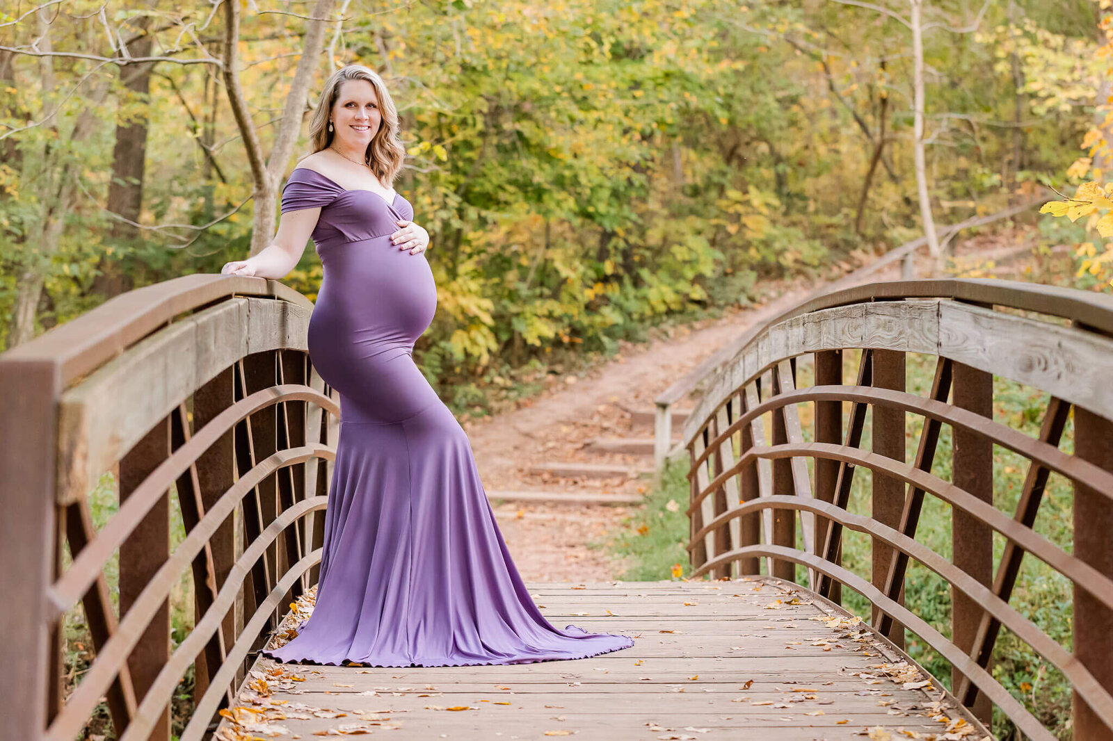A maternity portrait of a woman in a purple dress in a park.