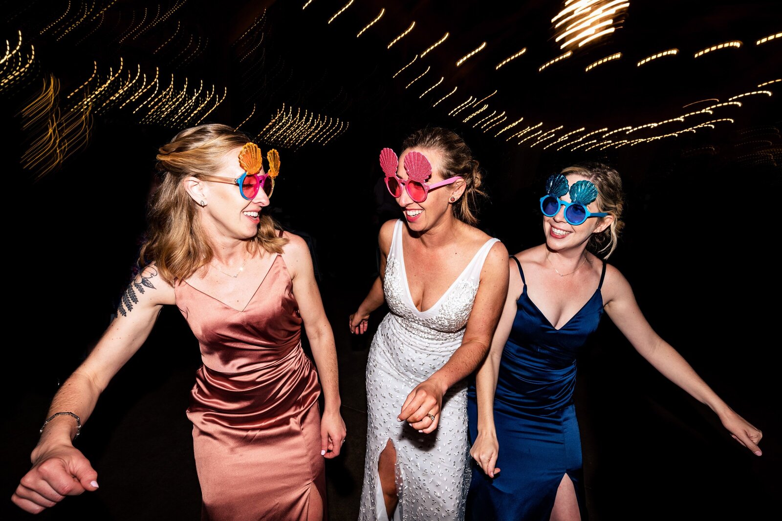 bride and two of her bridesmaids dancing on the dance floor in colorful sunglasses