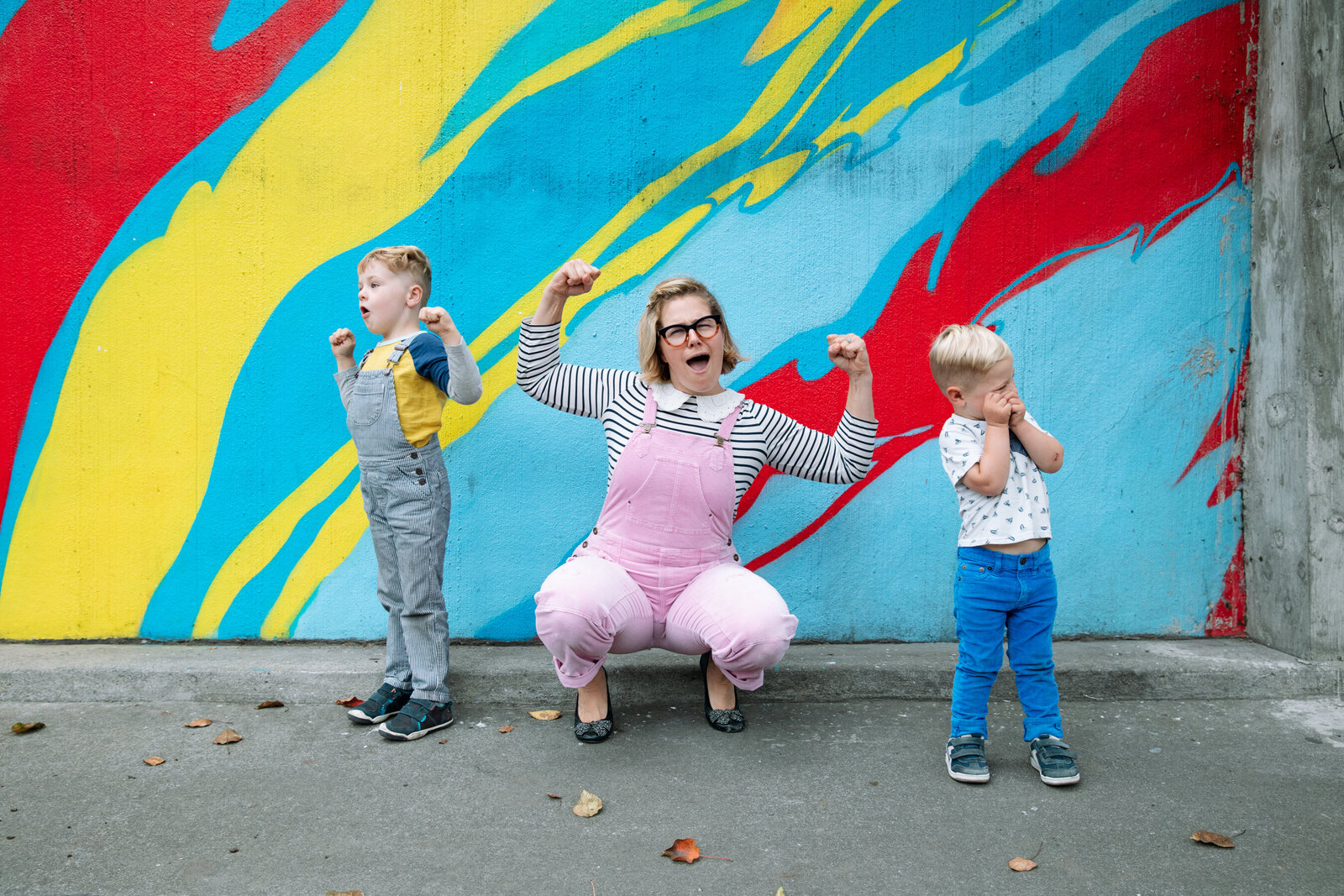 mom in pink overalls showing muscles with two young sons nearby