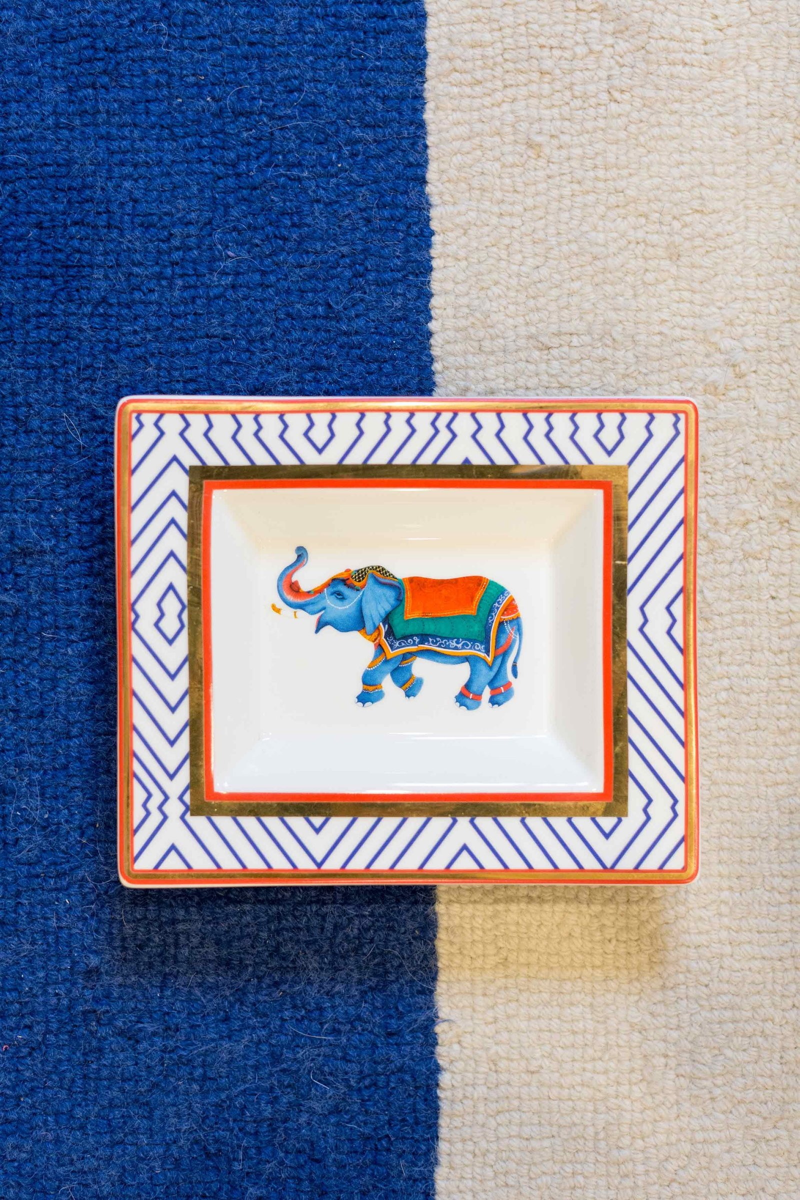A ceramic dish with an elephant on top of a blue and white rug.