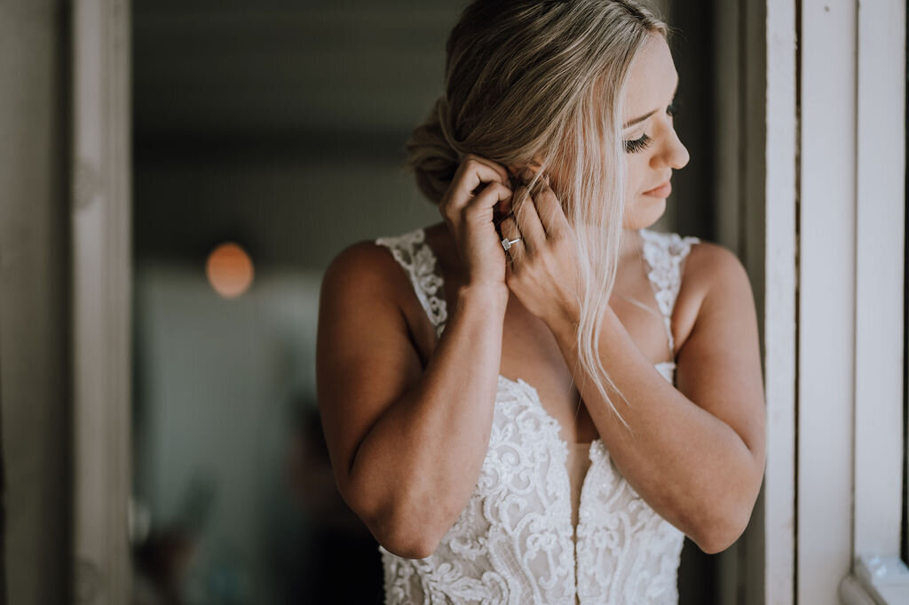 bride with blonde hair putting her earrings in