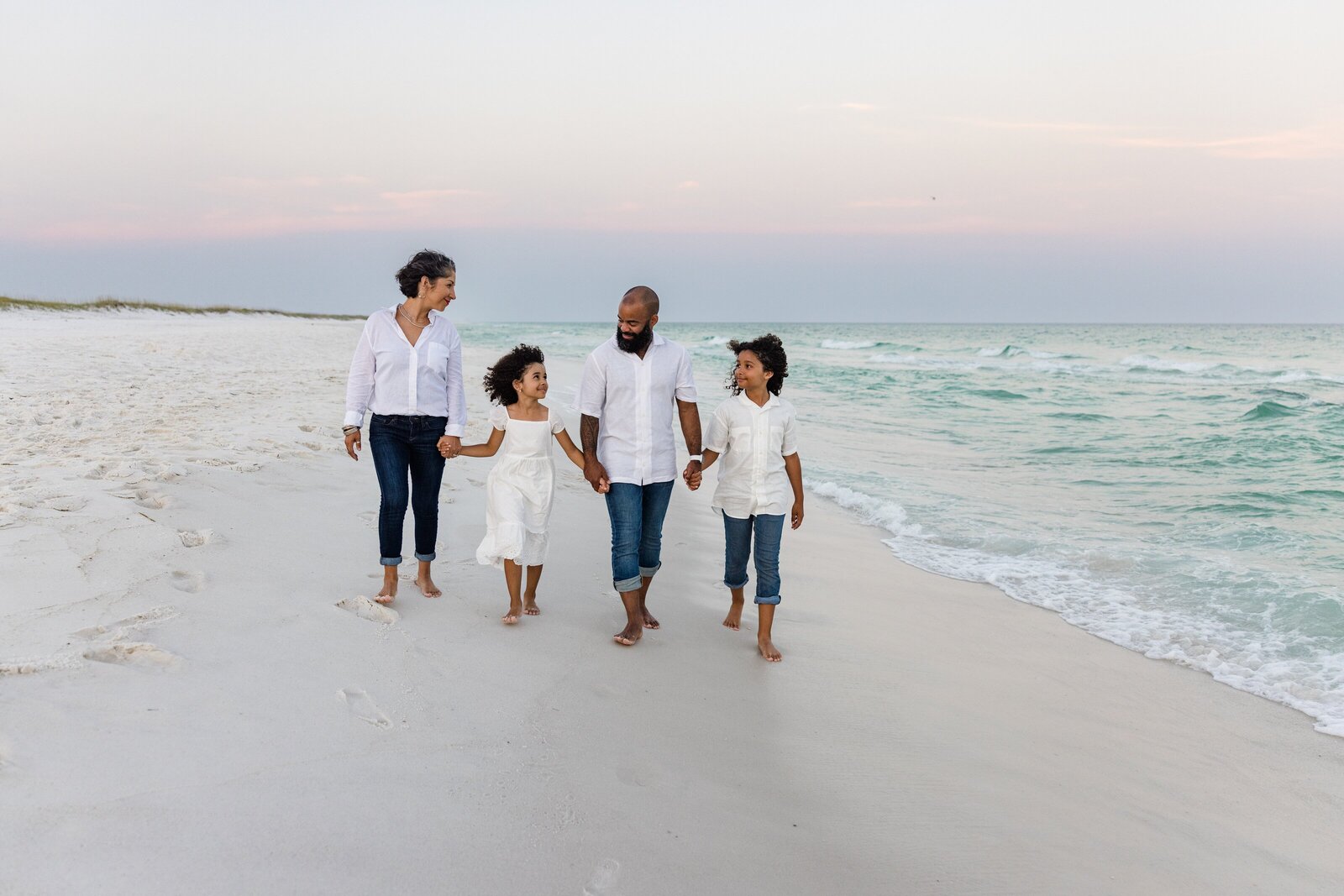 Family of 4 walking down Pensacola Beach holding hands at sunset