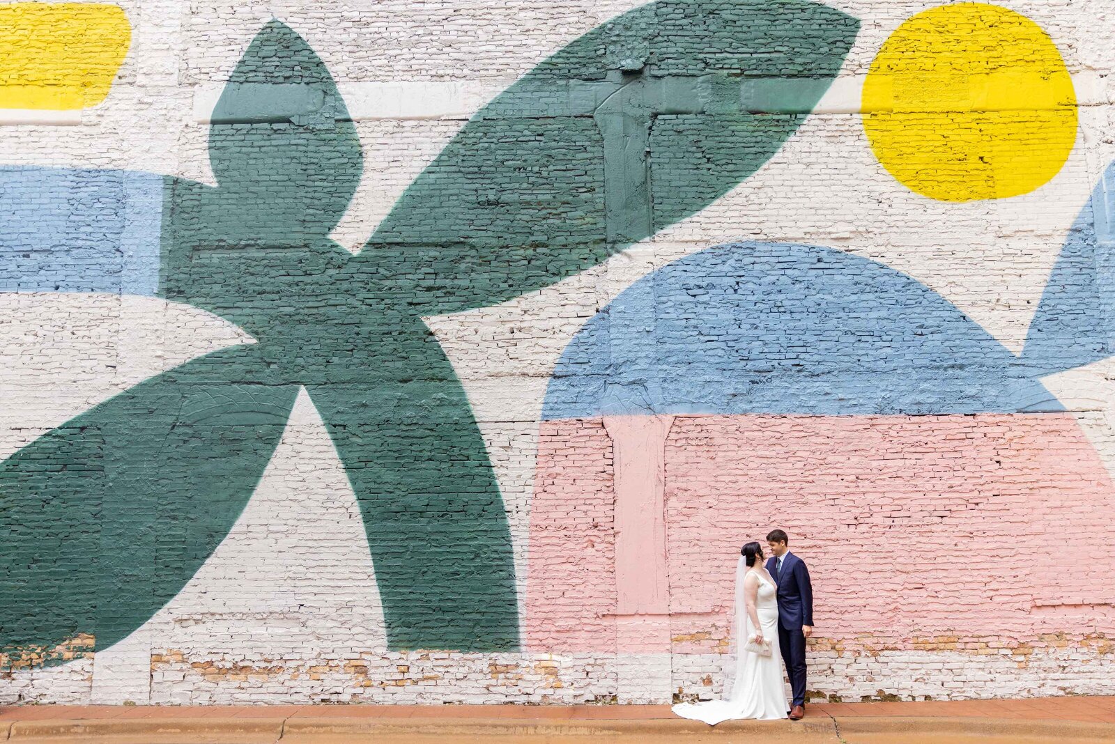 A wedding couple kissing in front of a large mural.