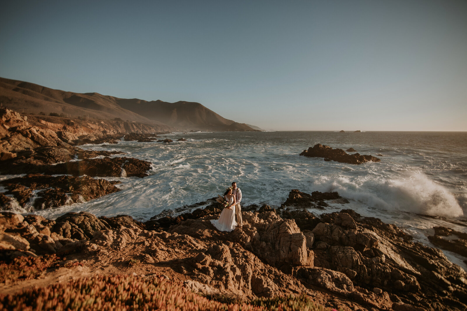 wedding couple standing on rocks with wild ocean