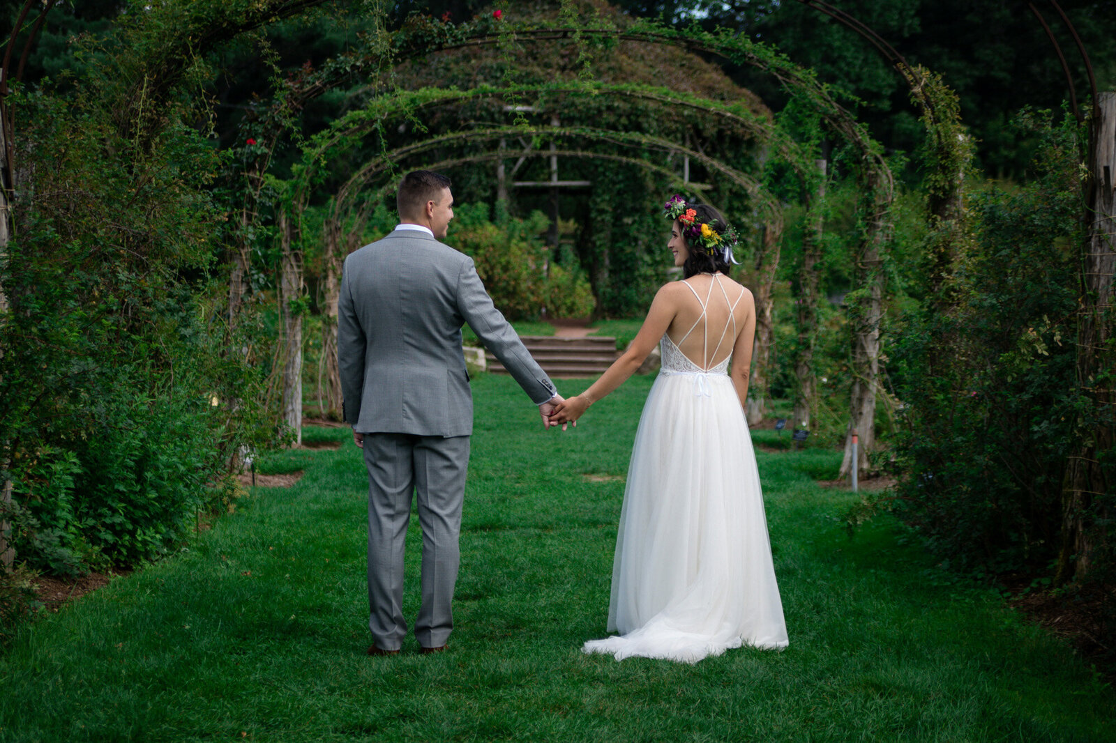 Bride and groom holding each other's hand while walking towards the pathway that has leaves and flowers arch
