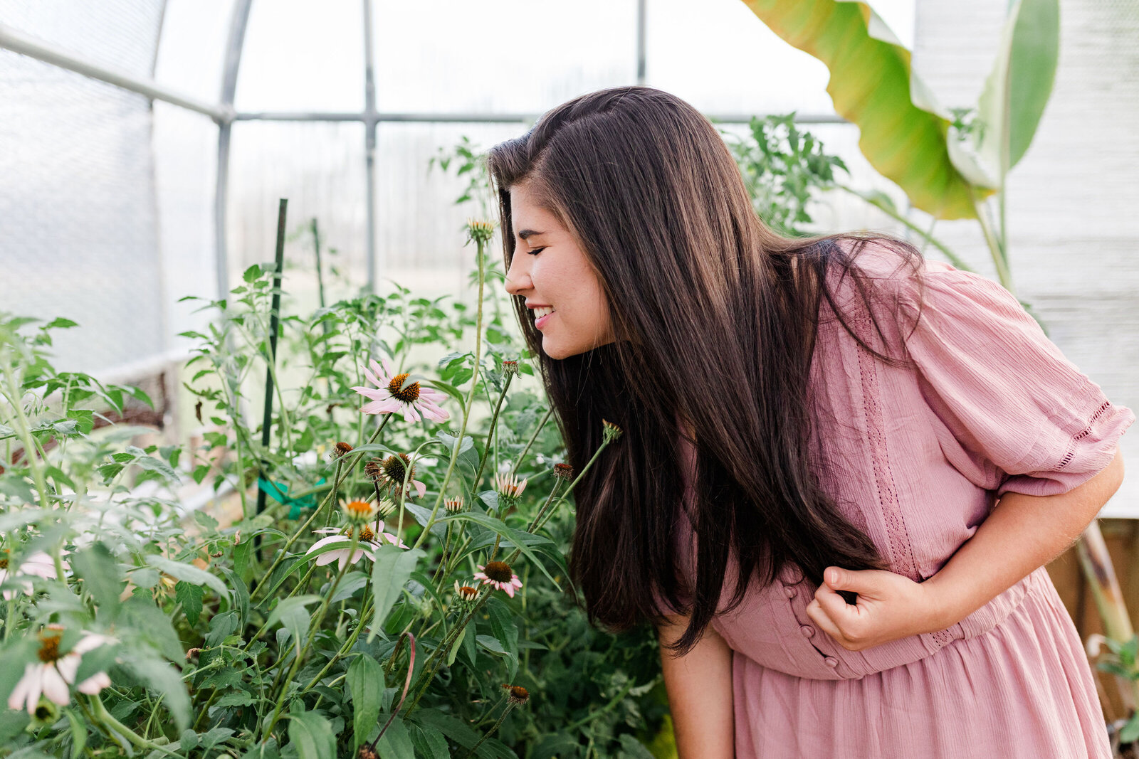High school senior smelling flowers in a greehouse