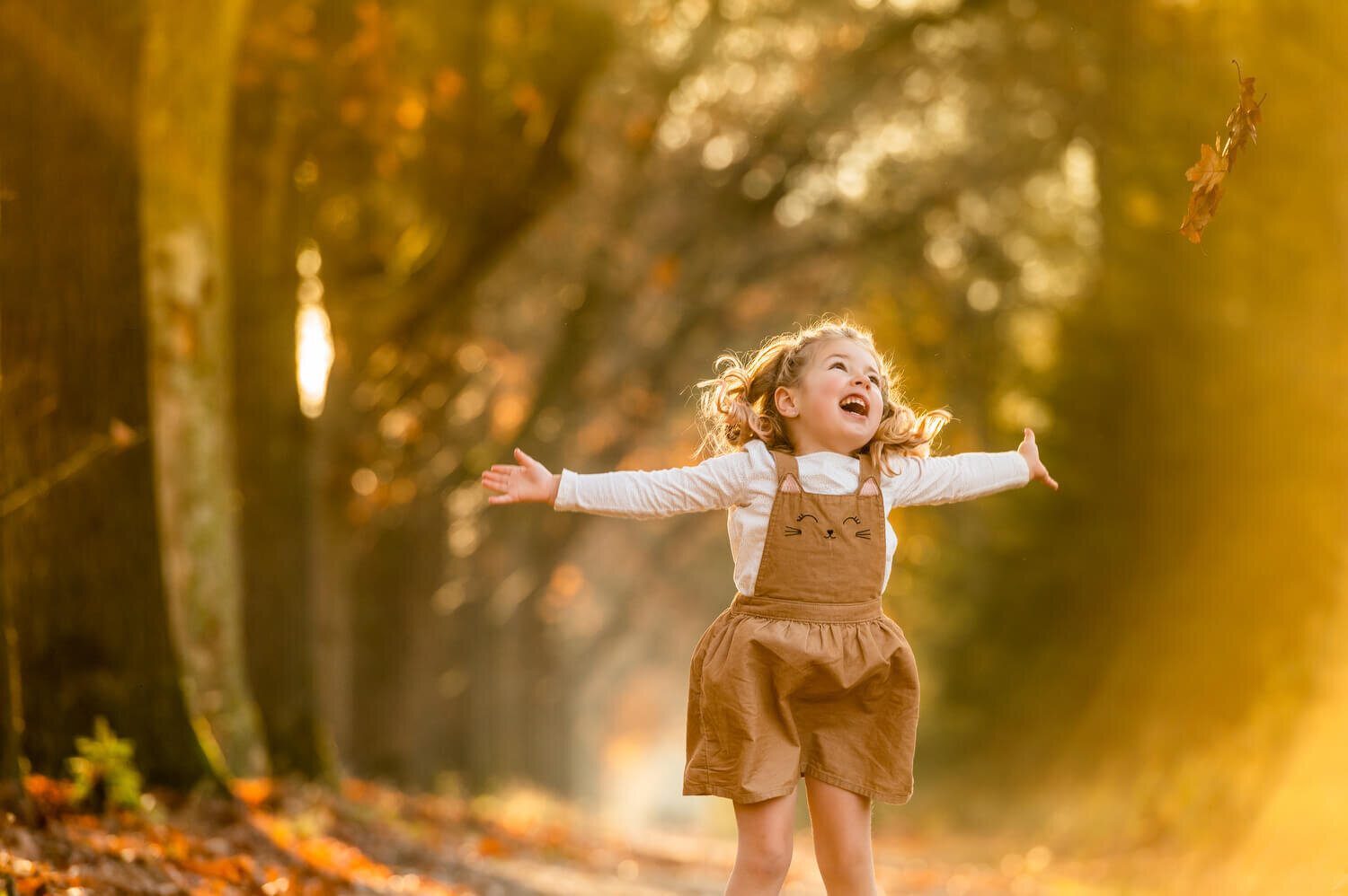 Herfstshoot met bladeren, zonnestralen en een vrolijk meisje
