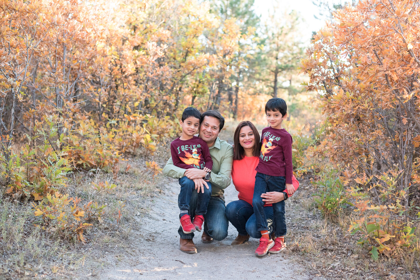 family outdoor photos with mom and dad crouched down with their two little children as they pose on a dirt trail in the mountains surrounded by fall trees captured by denver family photographers