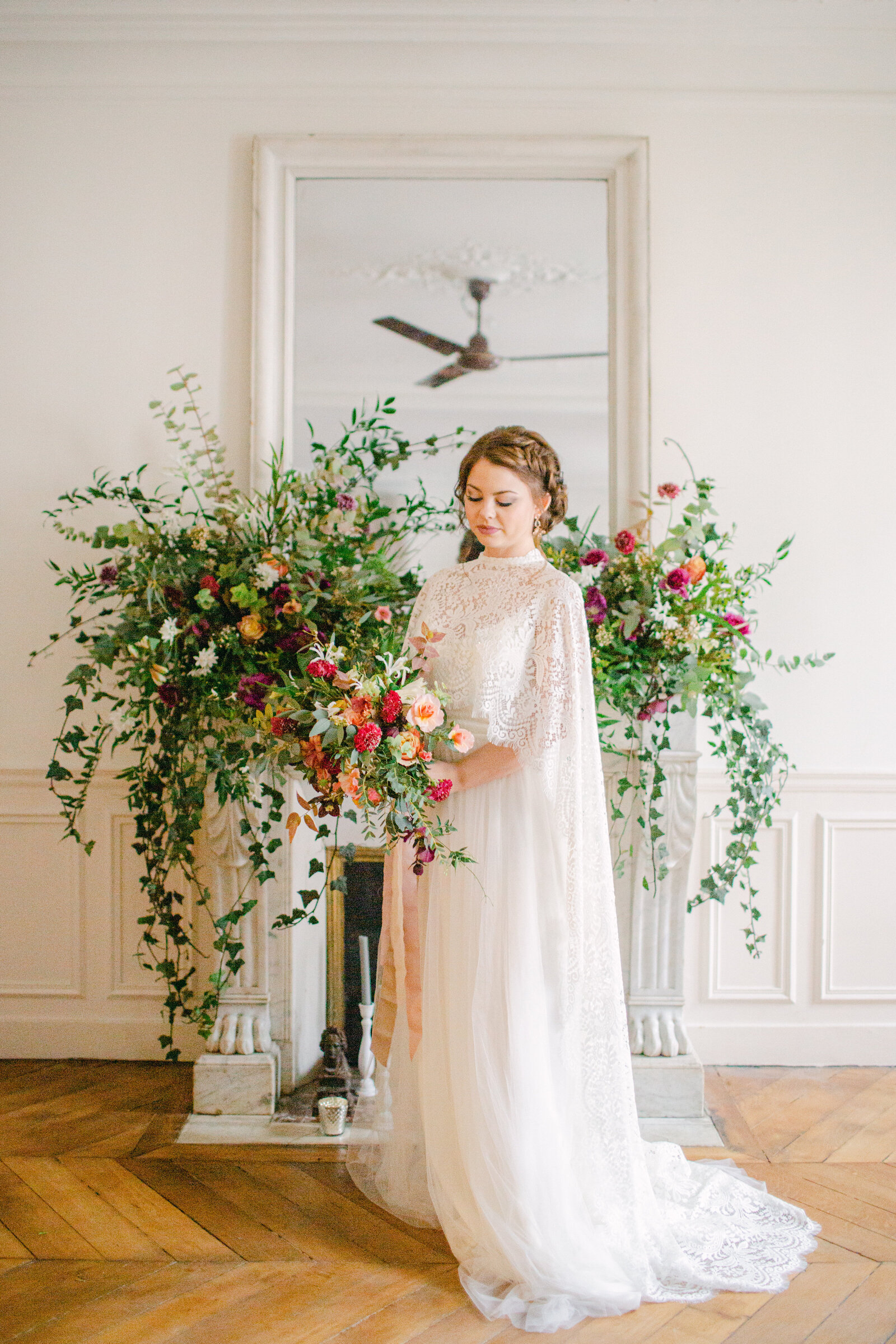 bride holding bouquet and standing in front of fireplace mantel with floral arrangement on it