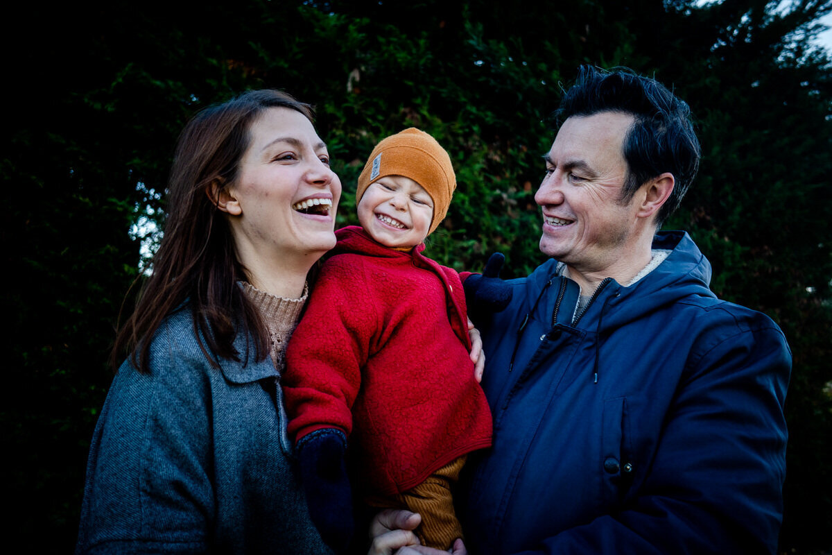fun laighing family during their portrait shoot in front of a conifer bush