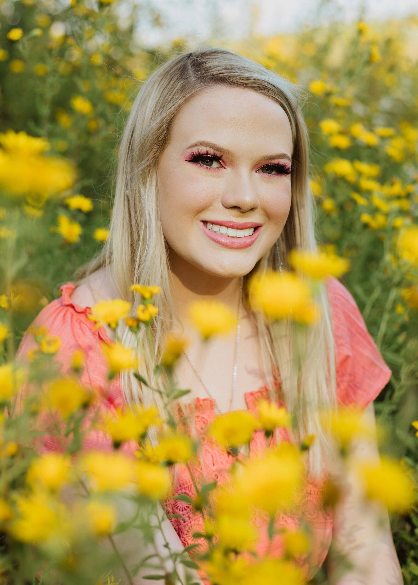 Senior girl smiling at camera, sitting in a field of yellow flowers