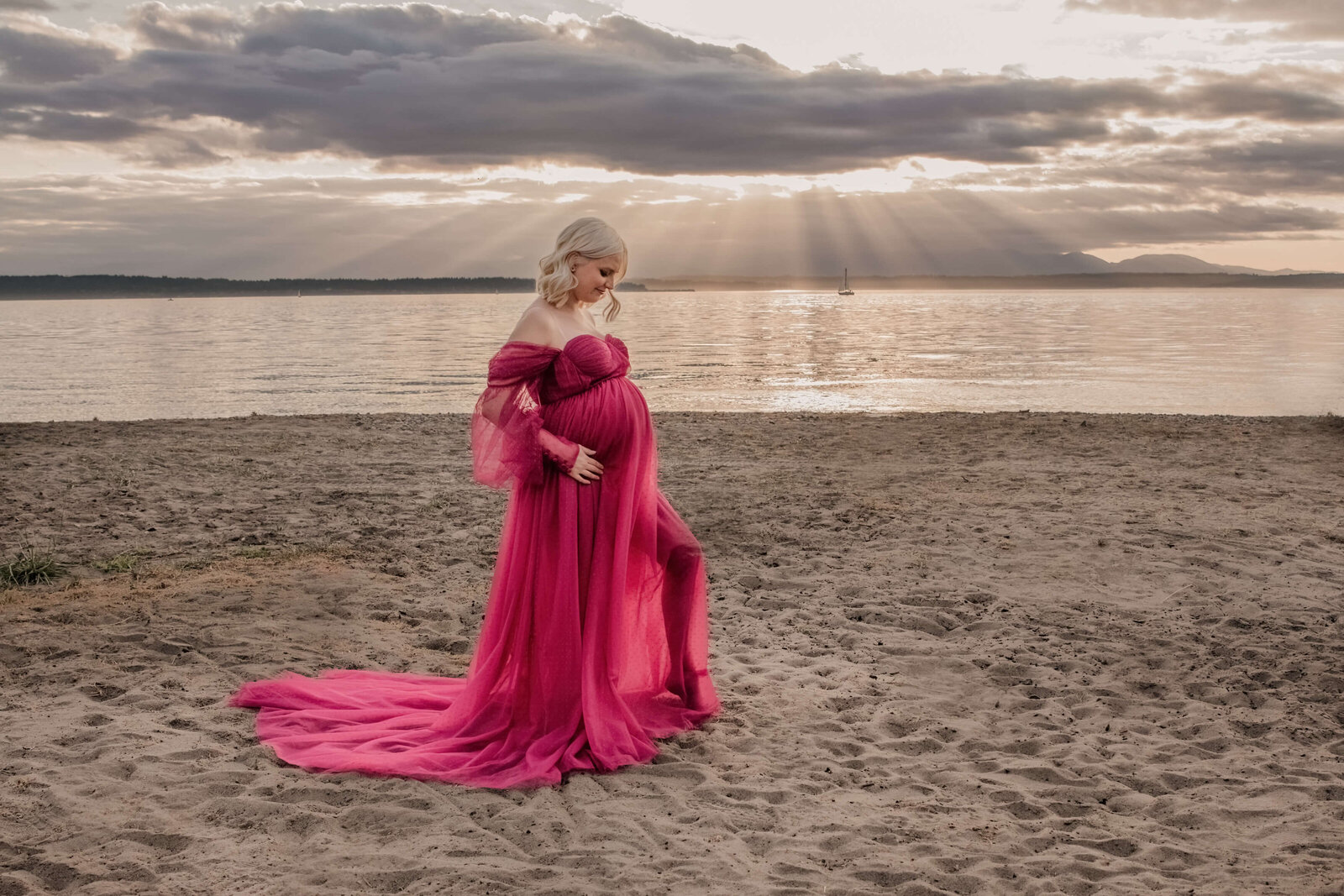 Pregnant woman in sheer dress on beach at sunset.