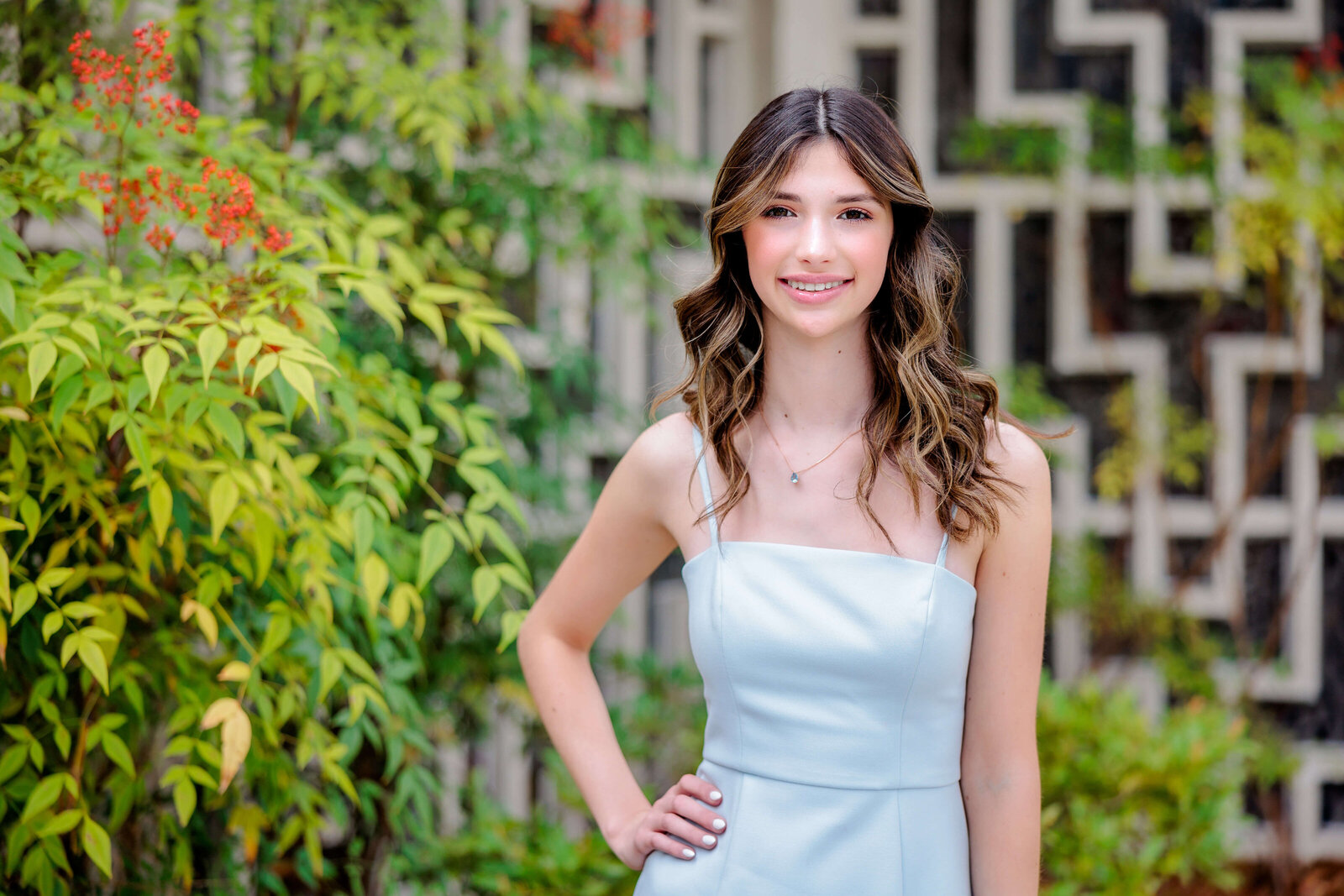 A teenage girl in a blue dress stands in a garden with a hand on her hip during a Bellevue Bar and Bat Mitzvah Photography session