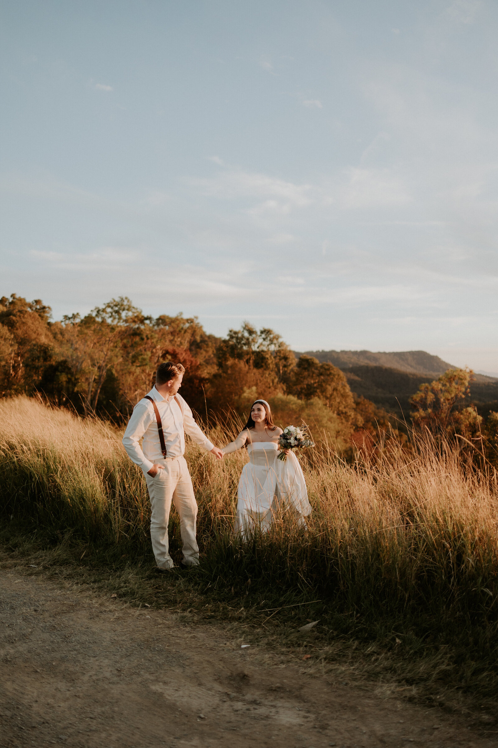 Bride and groom holding hands in long tall grass with mountain views
