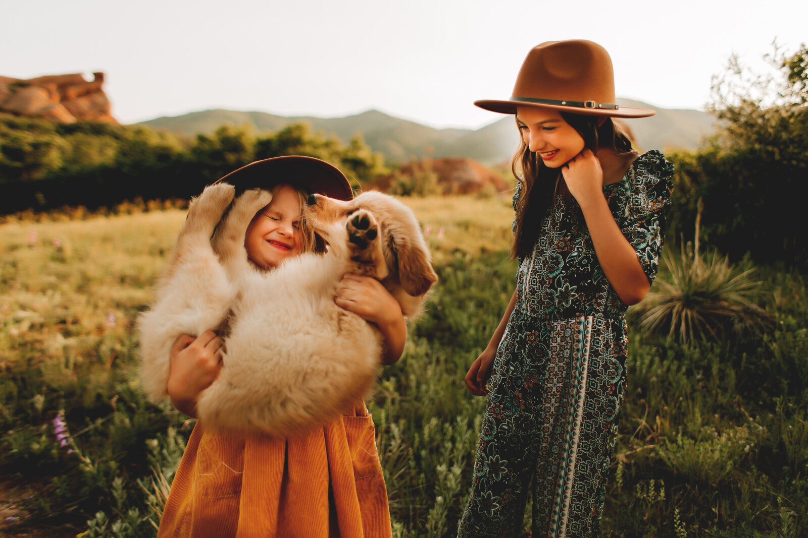 small girl holding  golden retreiver puppy with sister in grassy field in denver colorado during family session