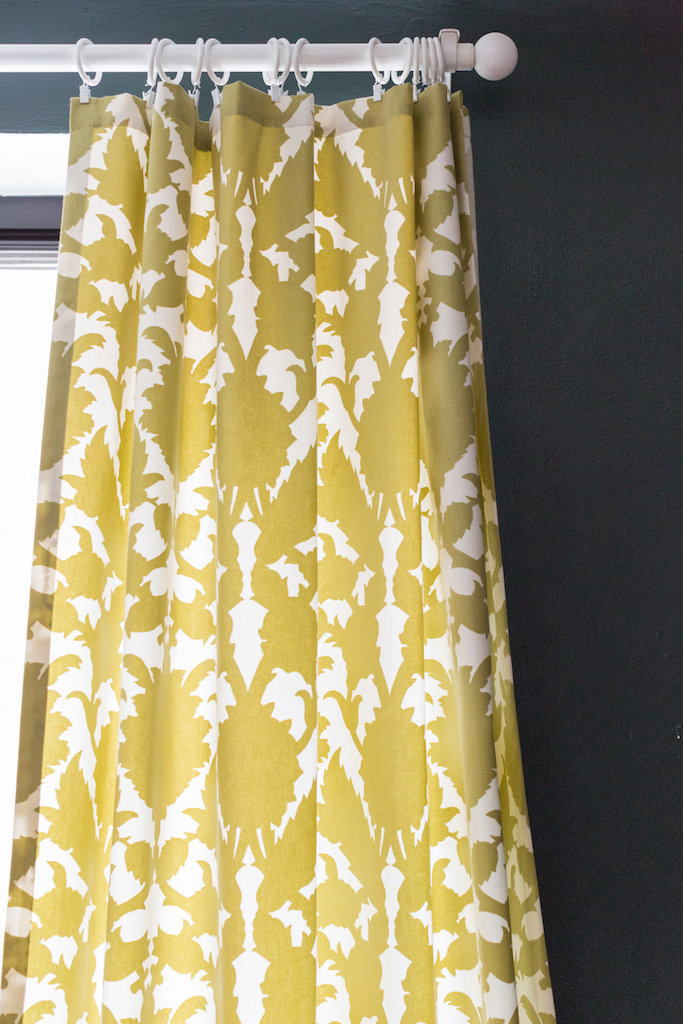 Yellow and white abstract patterned curtains against a dark green wall.