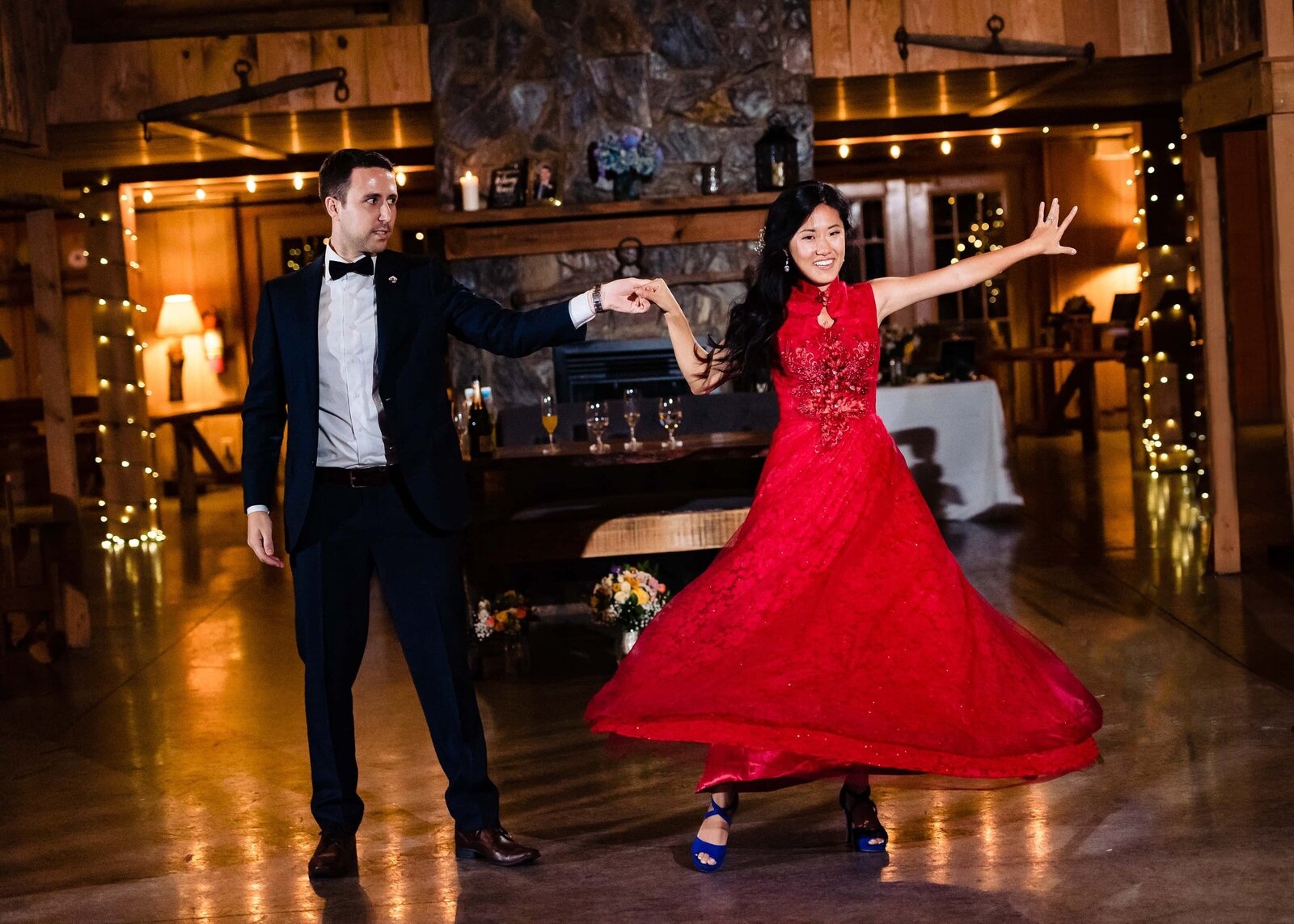 bride in a traditional red Chinese wedding dress twirls during her first dance; groom is wearing a black tuxedo