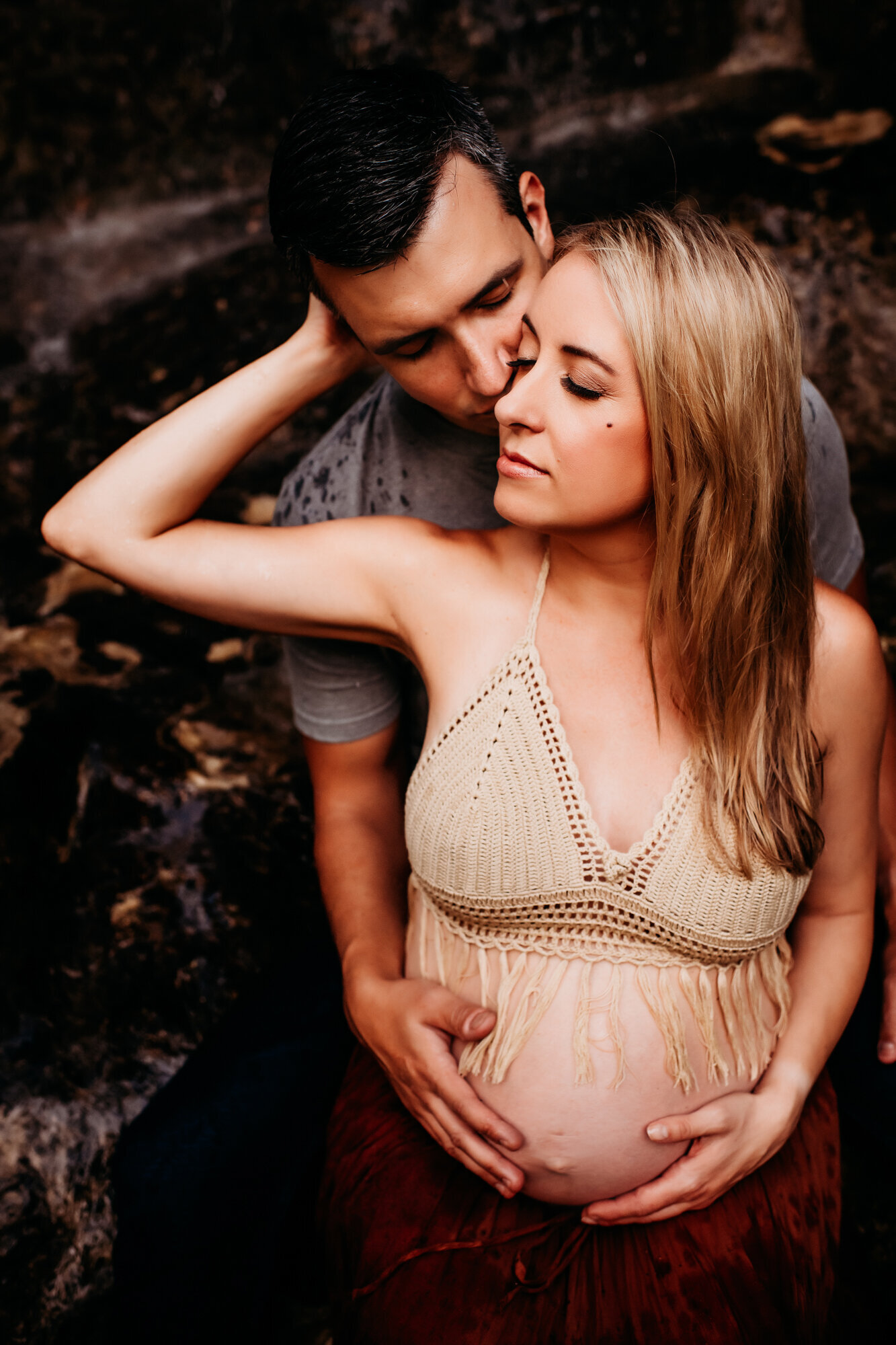 Maternity Photographer, Close up shot of man in a gray t shirt with woman leaning into him while his hands are on her pregnant belly.