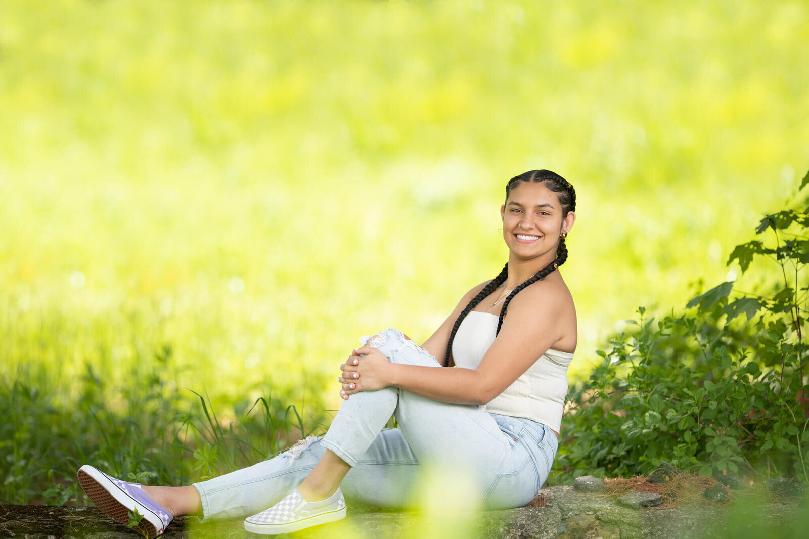 High school senior portrait photography in Clinton MA  of female in a white top smiling at the camera while sitting with a green and yellow background