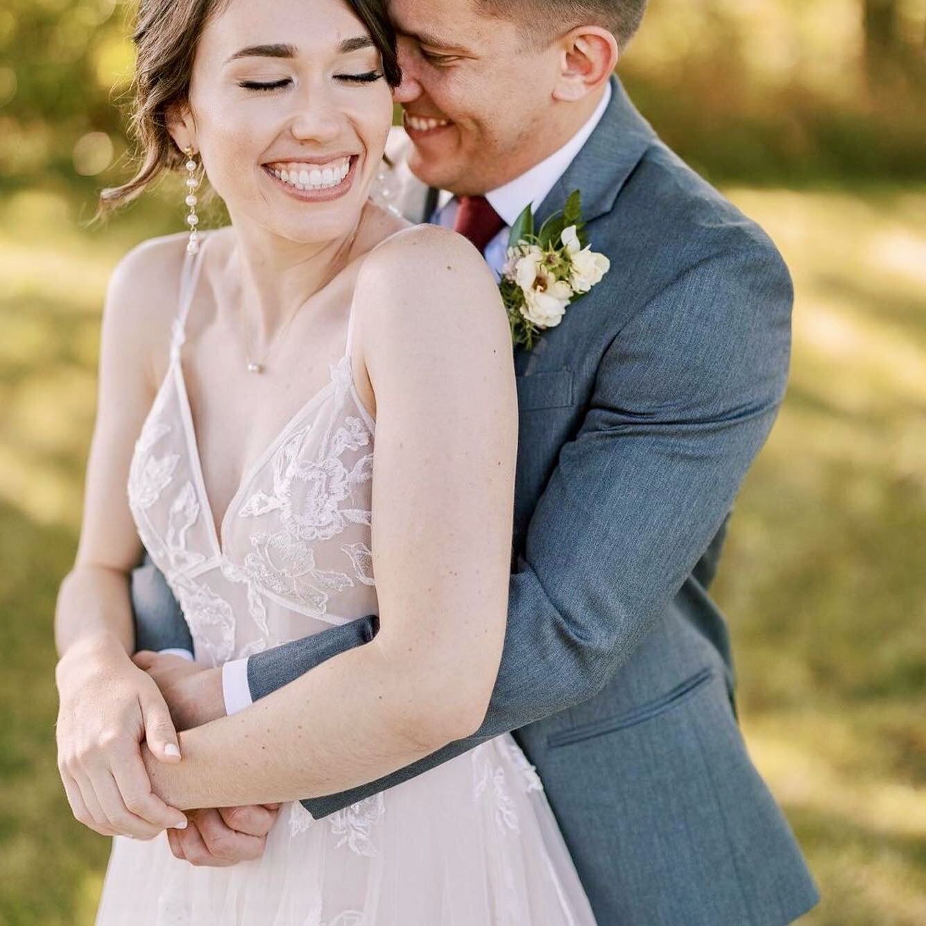 Groom embraces his bride from behind as they smile broadly on their wedding day