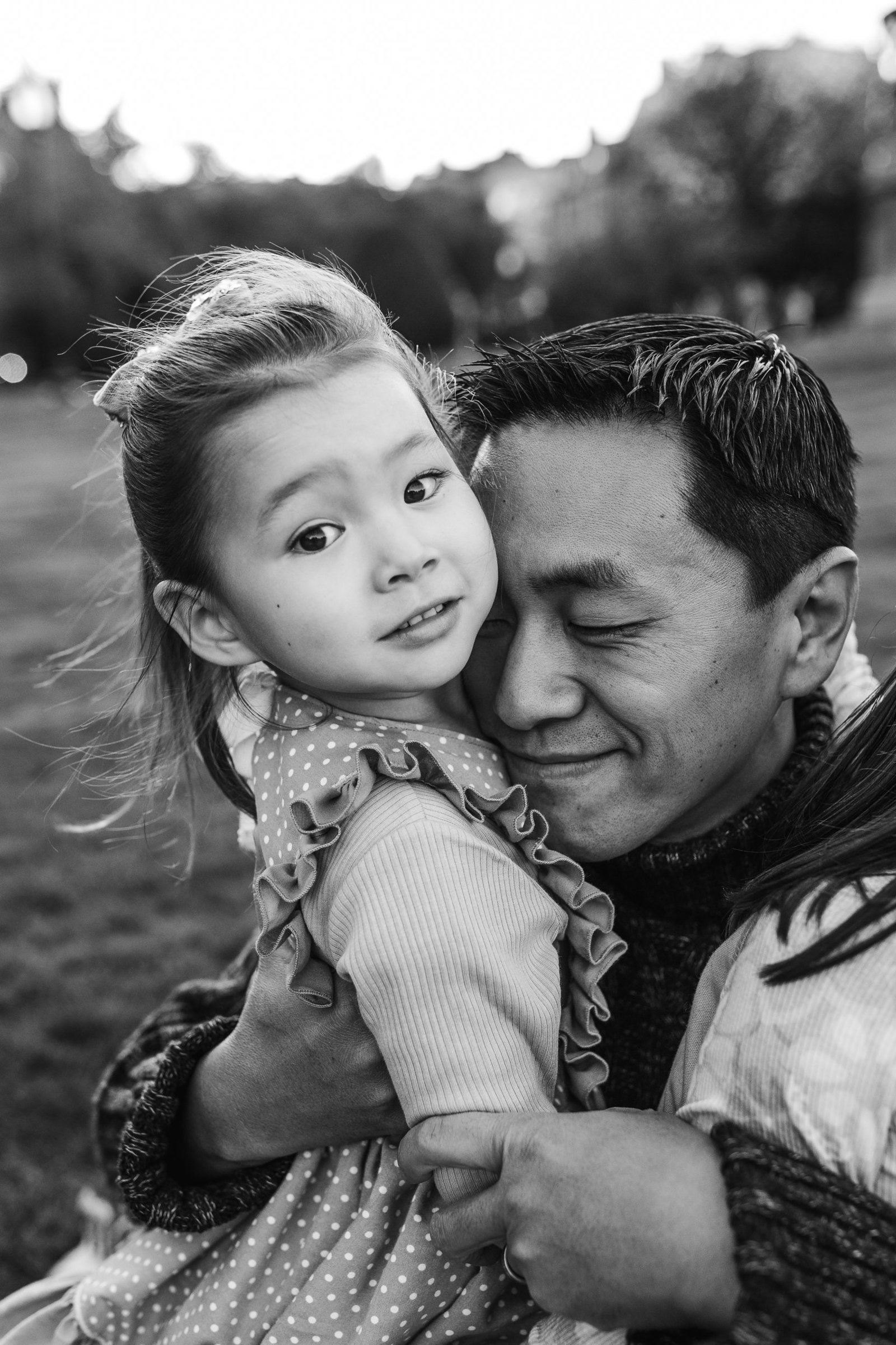 black and white portrait of father snuggling daughter who stares at camera in boston public garden