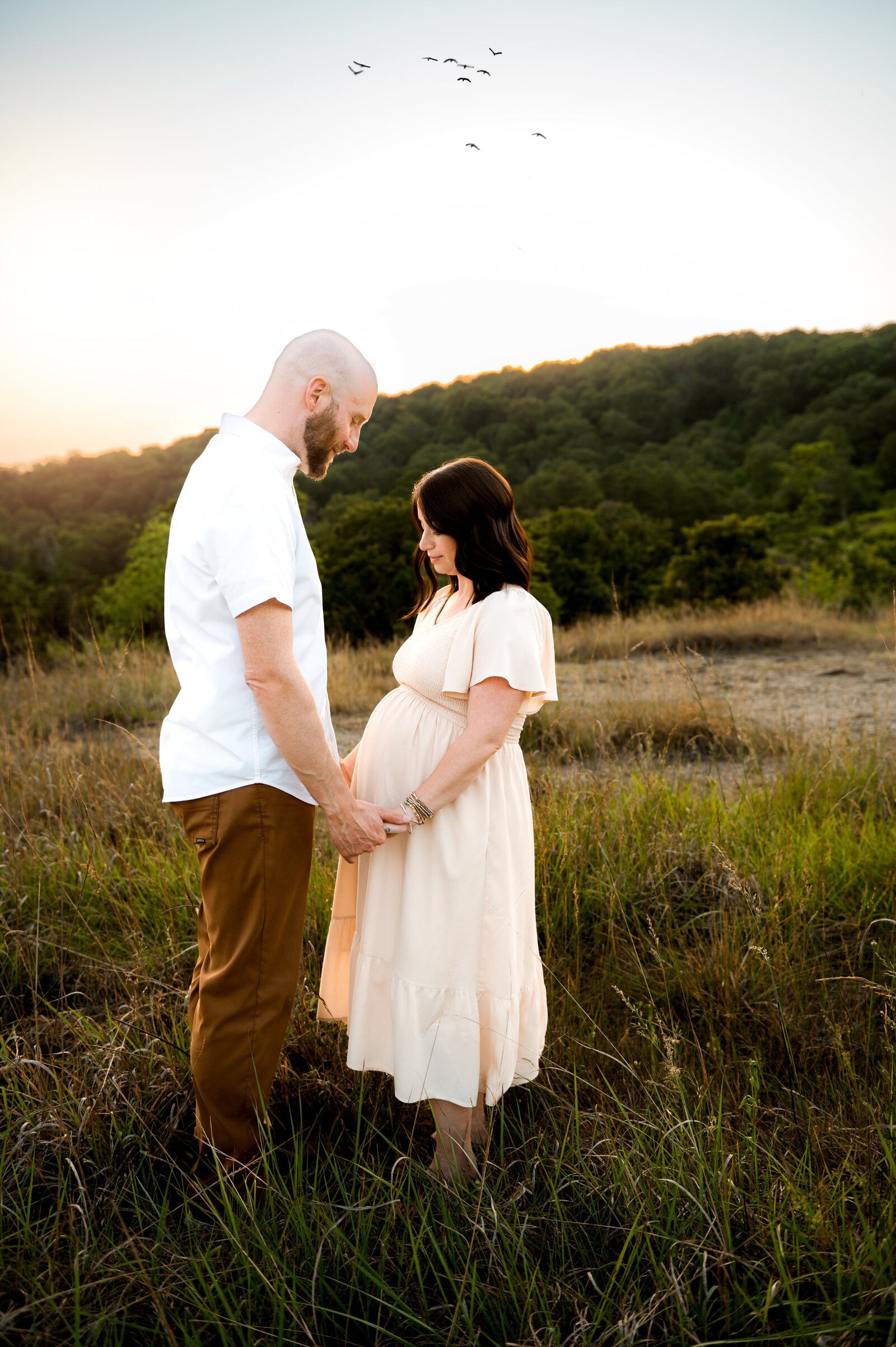 husband and wife in a field looking at pregnant belly