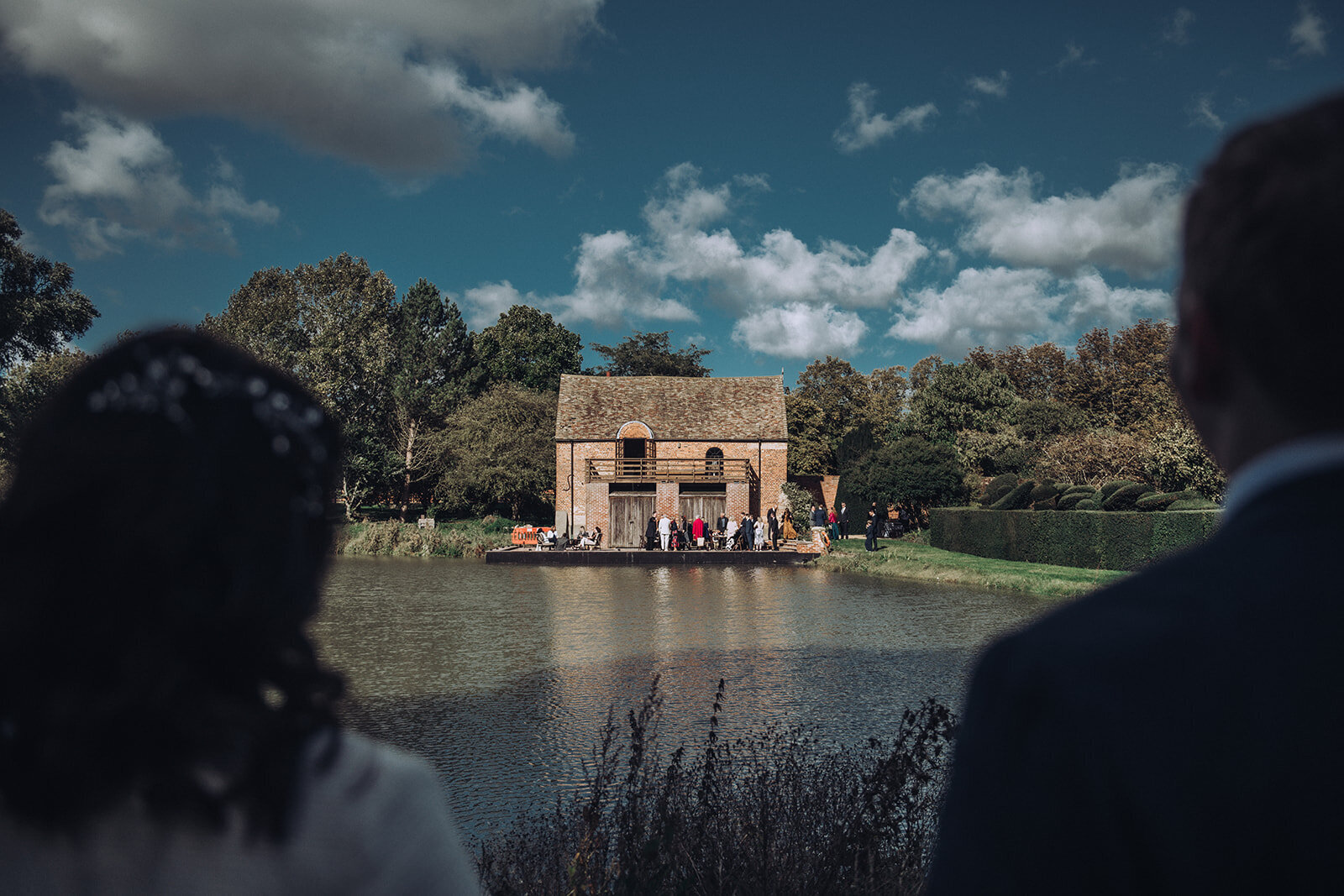 Bride and groom observing their friends and family from across a pond at their wedding at Childerley