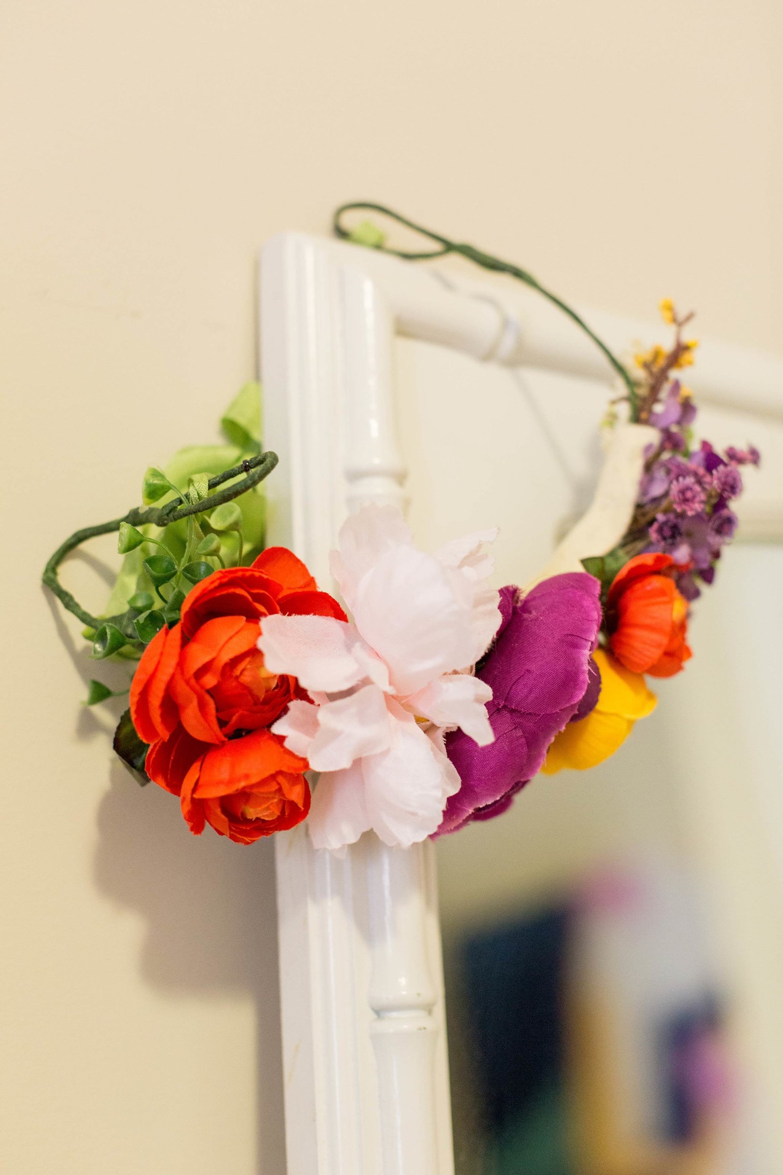 A bright flower crown hangs on the corner of a mirror.