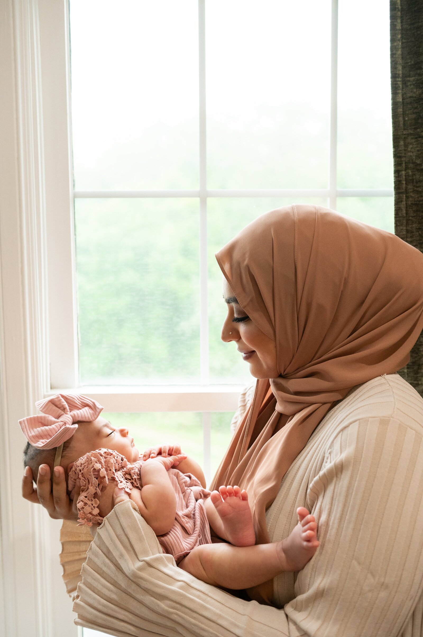 mom holding her newborn daughter by a window