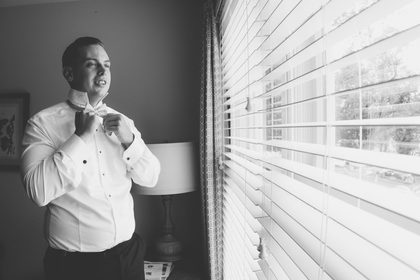 black and white photo of groom looking out the window at Three Village Inn