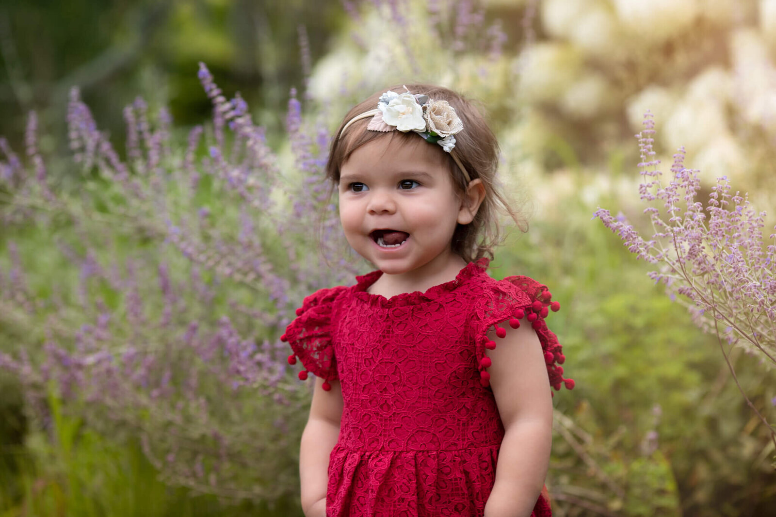 Little girl standing in front of purple flowers wearing red dress smiling