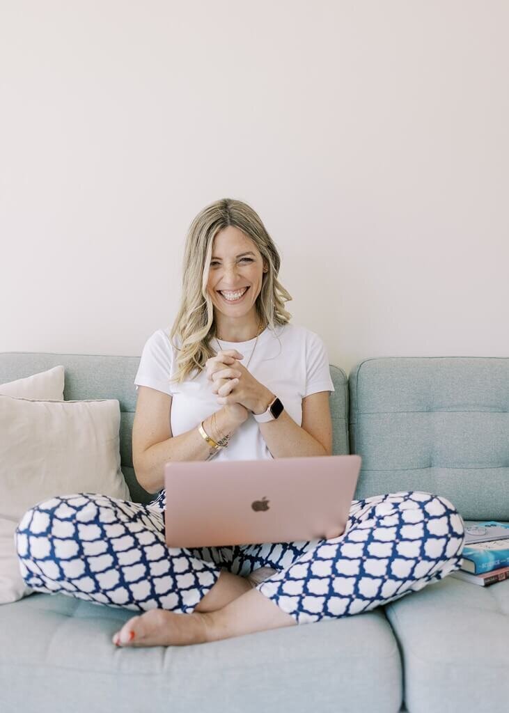 Women sitting on a blue sofa with her laptop in her lap smiling for her brand photoshoot.