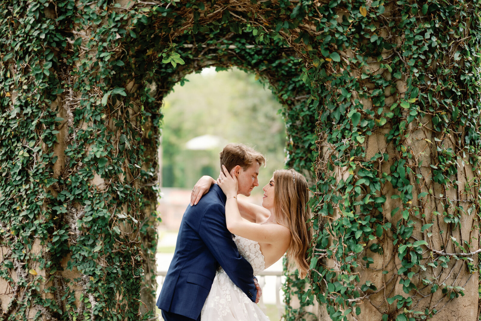 Groom leaning over slightly to kiss his bride in a ivy covered garden archway