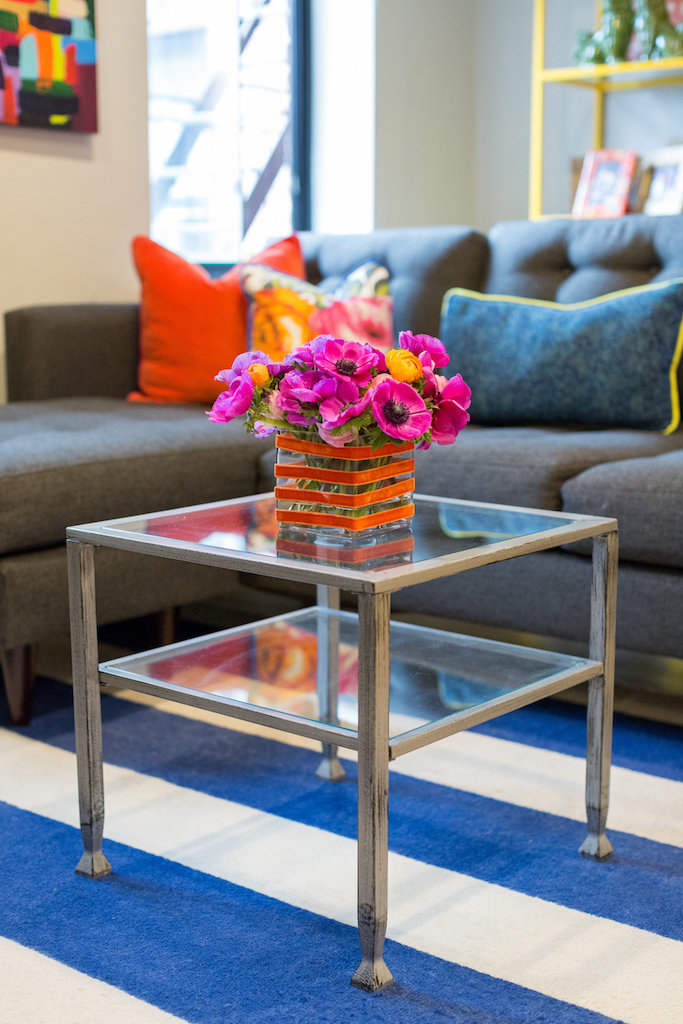A metal and glass coffee table with an orange vase and pink flowers.