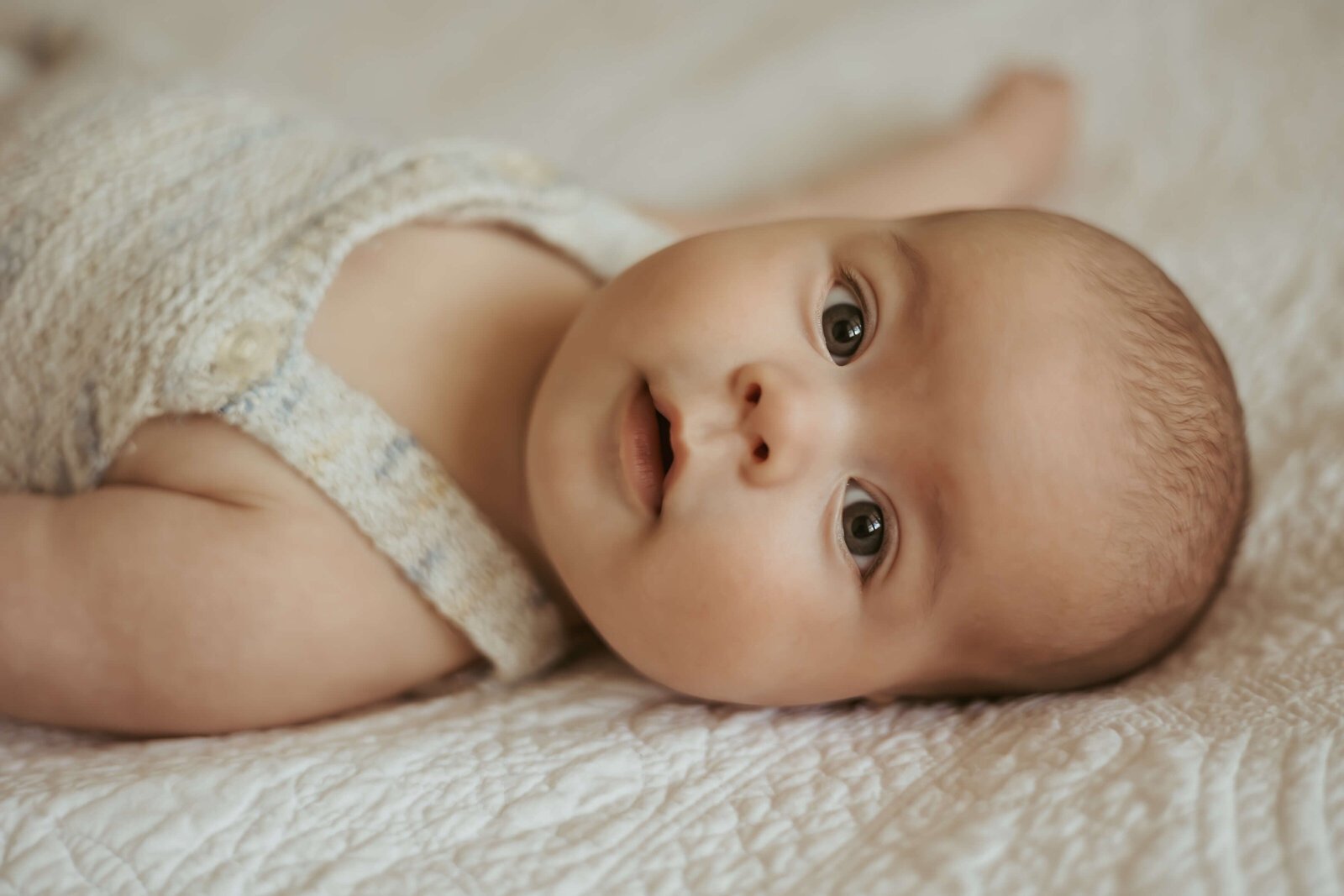 A close up photograph of a four month old baby on his parent's bed staring into the camera.