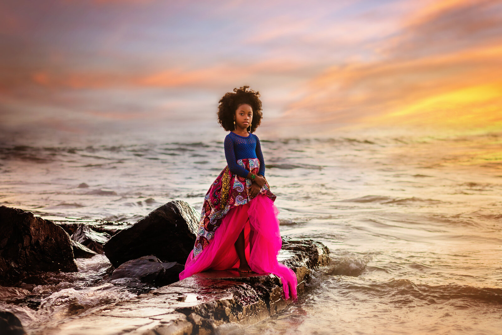 Family Photographer, a young girl stands on rocks near the ocean