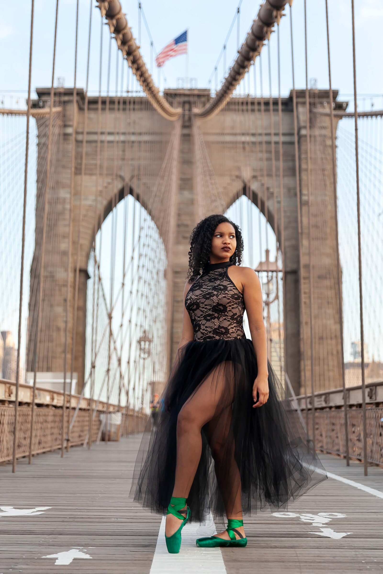 Black curly haired ballerina in romantic tutu and green pointe shoes posing on the Brooklyn Bridge
